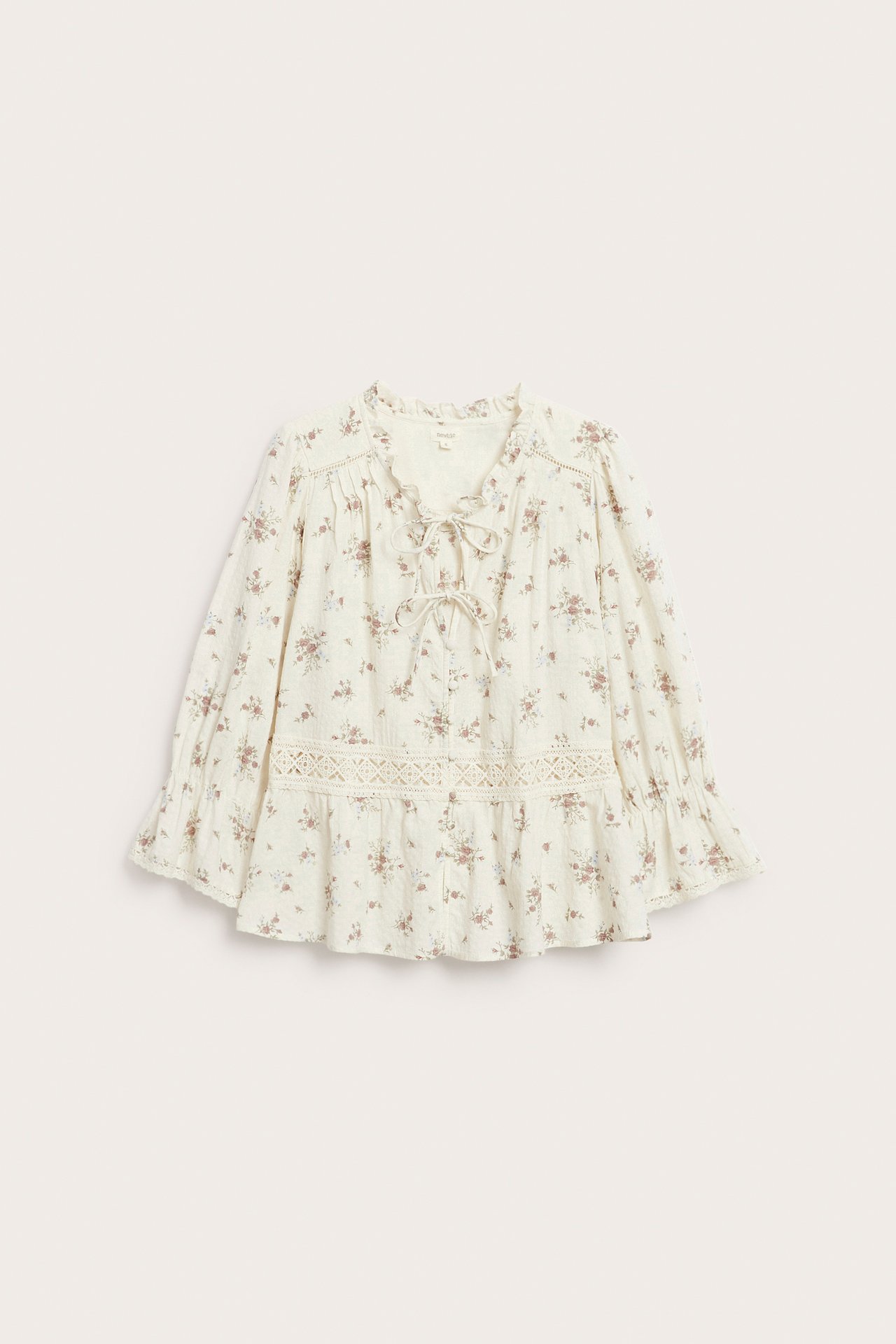 Framsida av en benvit blommig bomullsblus med peplum, spetsdetaljer, v-ringning och knytband.