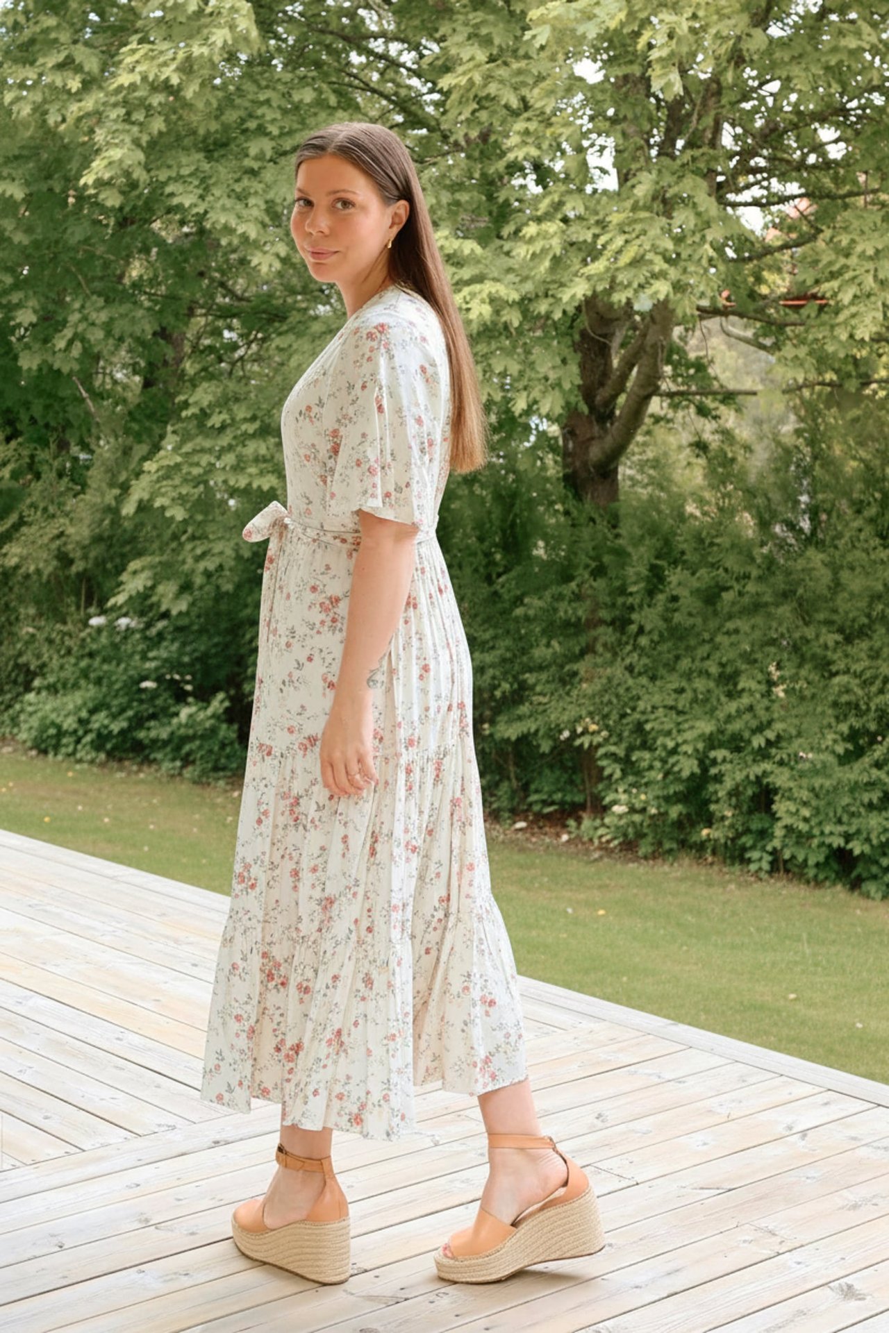 Sida vy av kvinna i offwhite blommig viskosklänning med knytbälte och beiga kilklackssandaler.