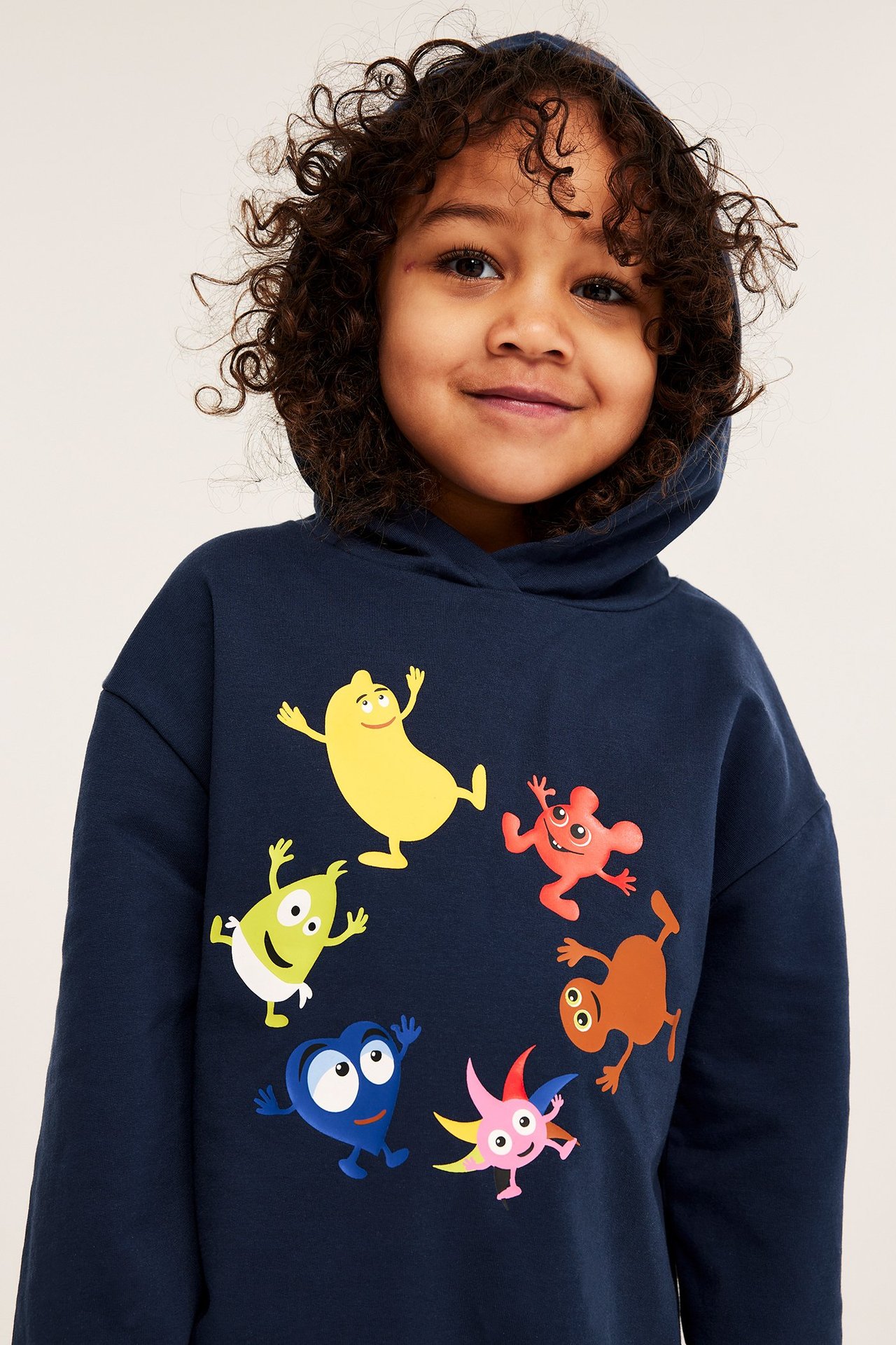 Front view av ett leende barn i en mörkblå bomullshoodie med Babblarna-tryck.