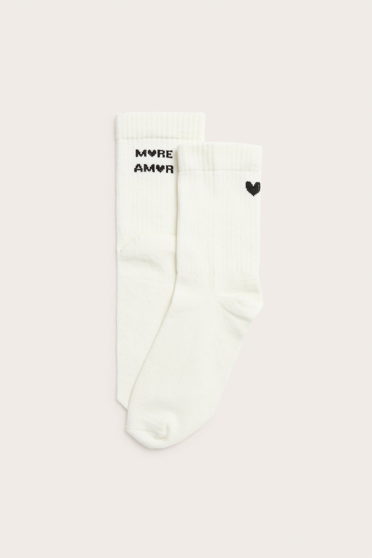 Widok z góry na dwie kremowe prążkowane skarpetki: jedna z czarnym napisem 'MVRE AMVR', druga z sercem.
