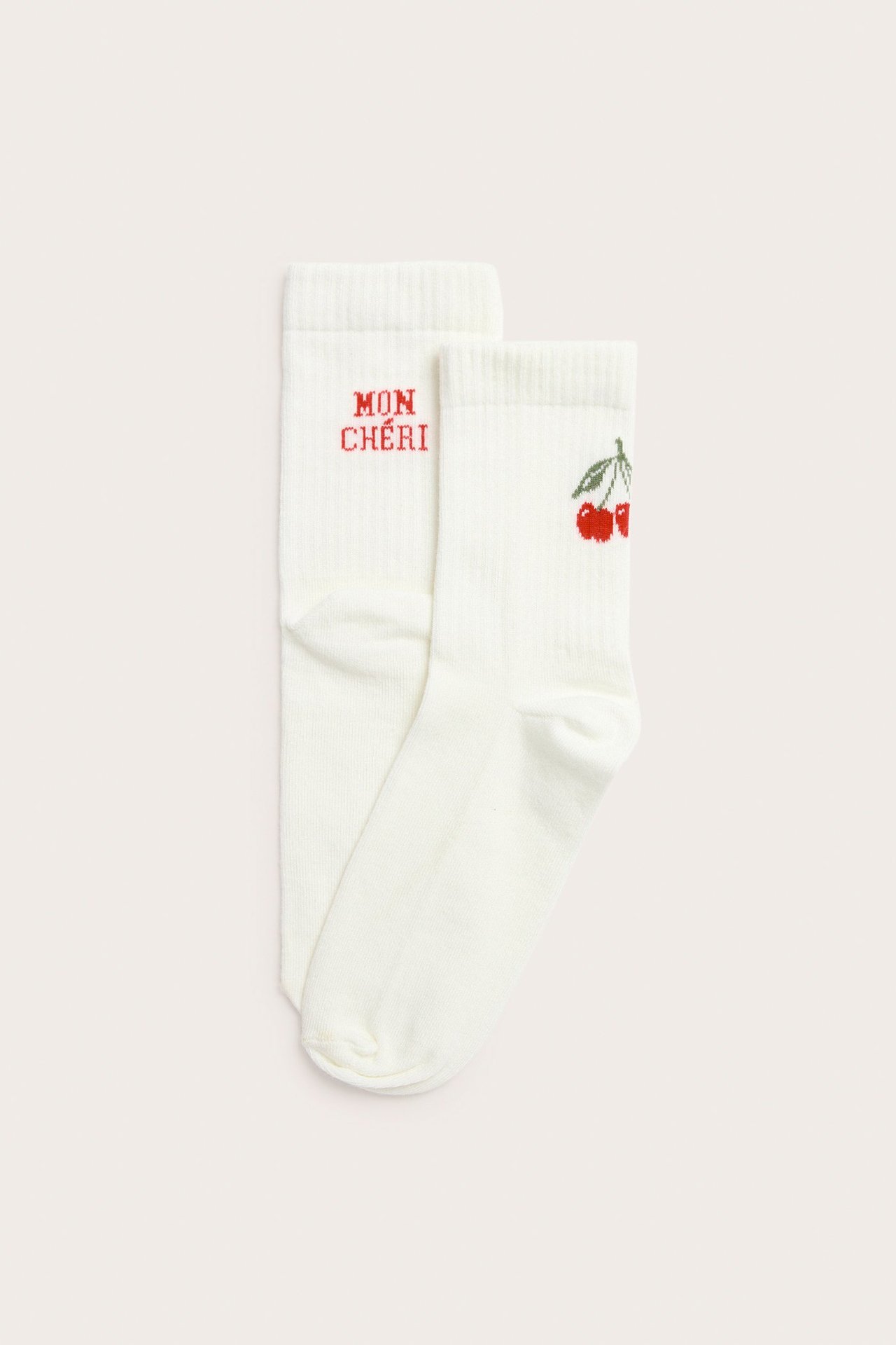 Widok z góry na dwie kremowe skarpetki; jedna z czerwonym napisem 'MON CHÉRI', druga z haftem wiśni.