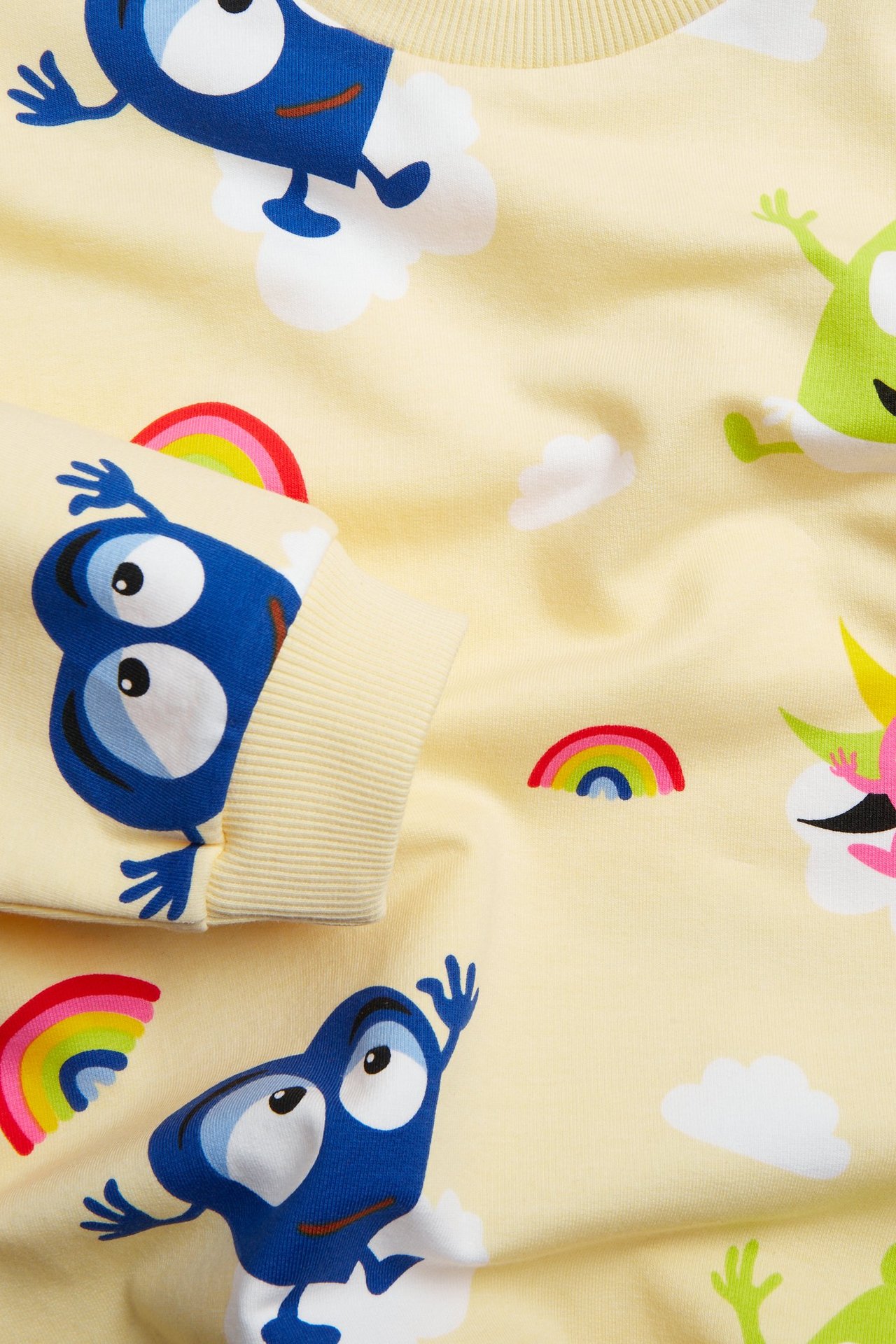 Zbliżenie na jasnobeżową bluzę dziecięcą z kolorowym wzorem Babblarna, chmurkami i prążkowanym mankietem.