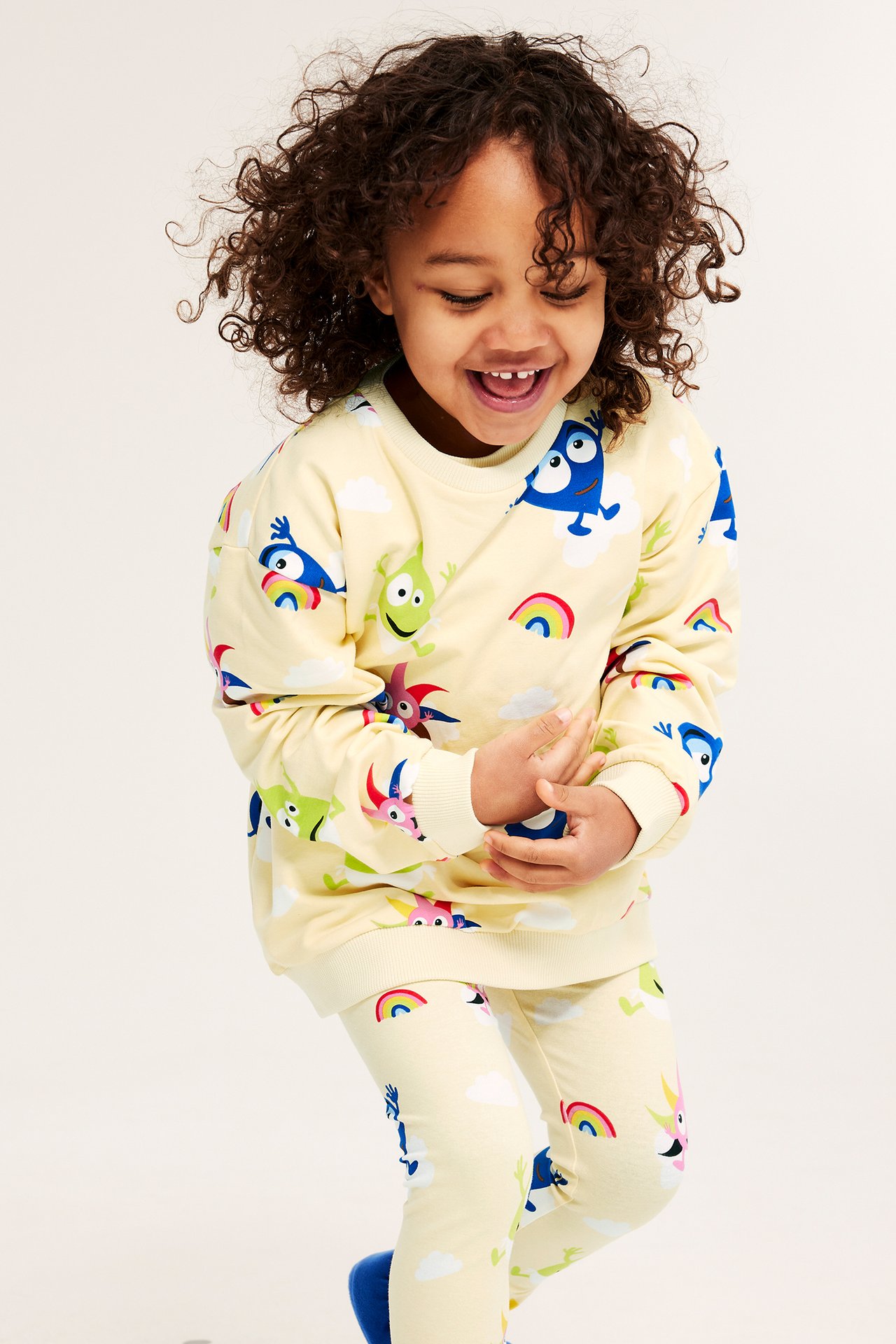 Uśmiechnięte dziecko z przodu w jasnobeżowej bluzie dresowej Babblarna we wzory i pasujących legginsach.