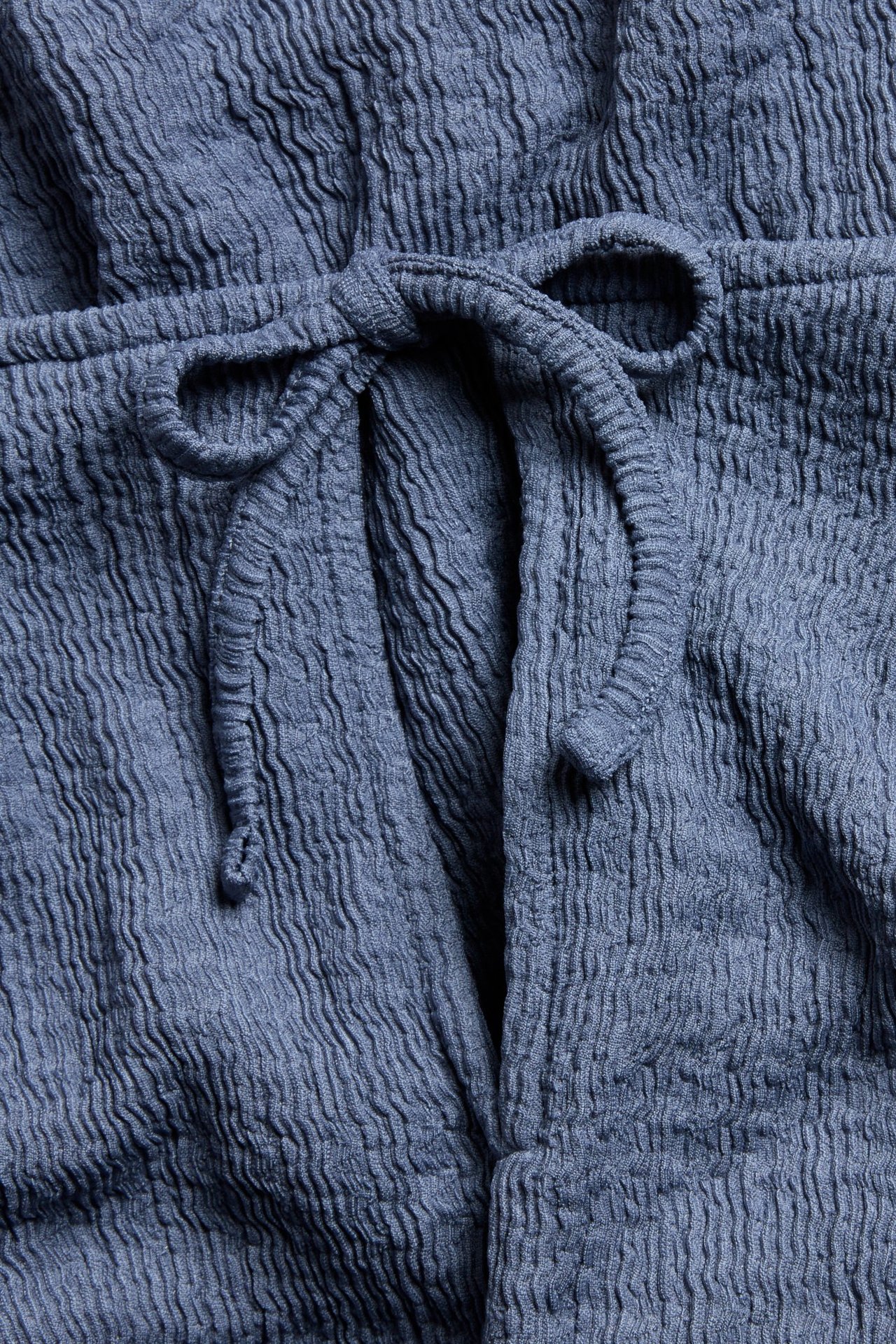 Zbliżenie niebieskiego topu z teksturowanej tkaniny z wiązaniem.