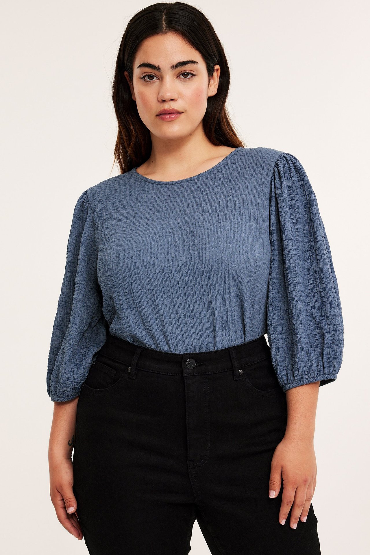 Widok z przodu: kobieta w niebieskim teksturowanym topie z bufiastymi rękawami i czarnych jeansach.