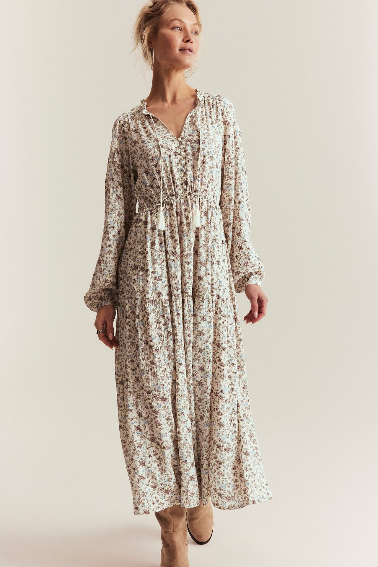 Frontutsikt: Kvinne i offwhite blomstret kjole med volang V-hals, knytebånd og elastisk midje.