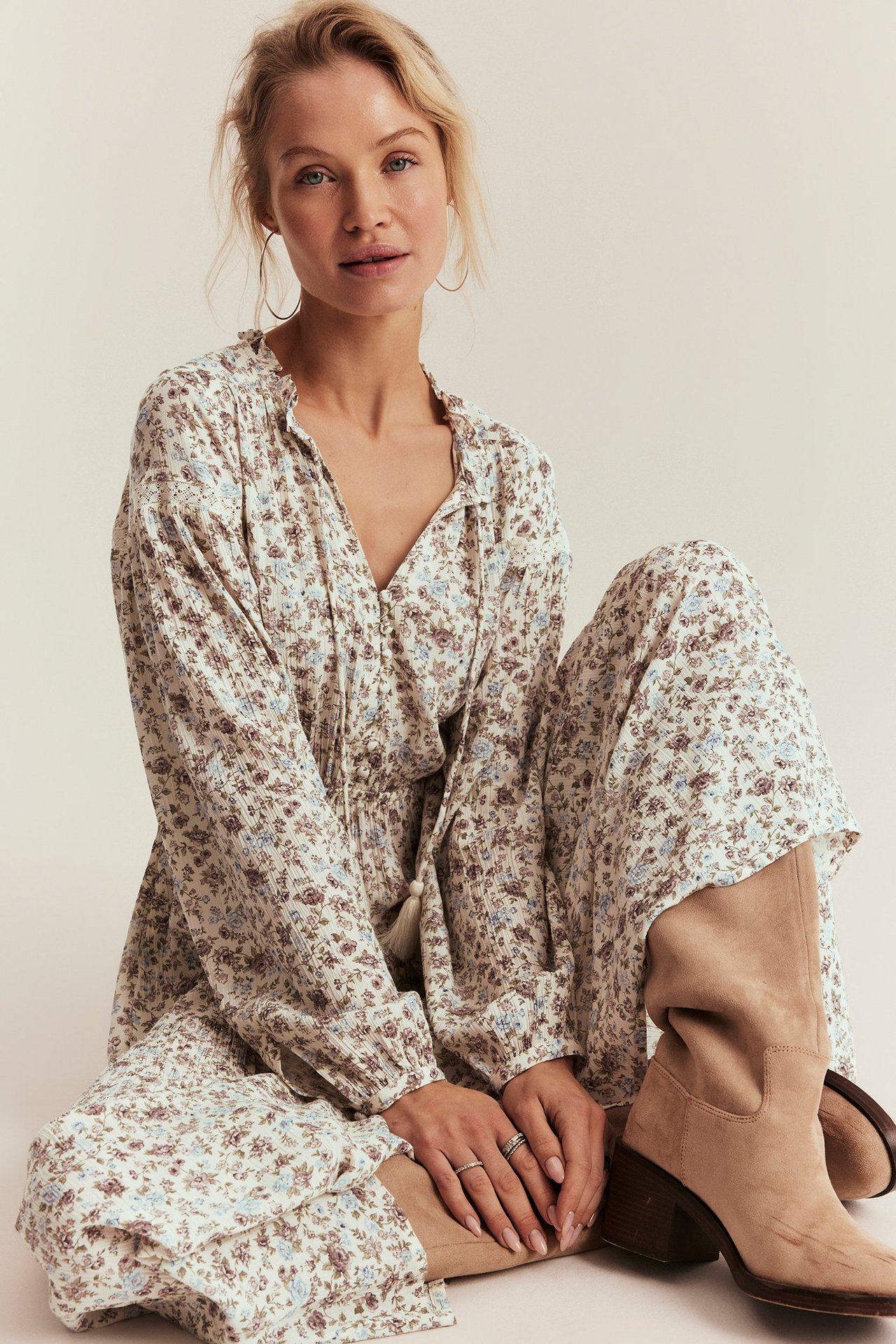 Widok z przodu, kobieta w kremowej kwiecistej wiskozowej sukience maxi z falbanką, wiązaniami i beżowymi zamszowymi kozakami.