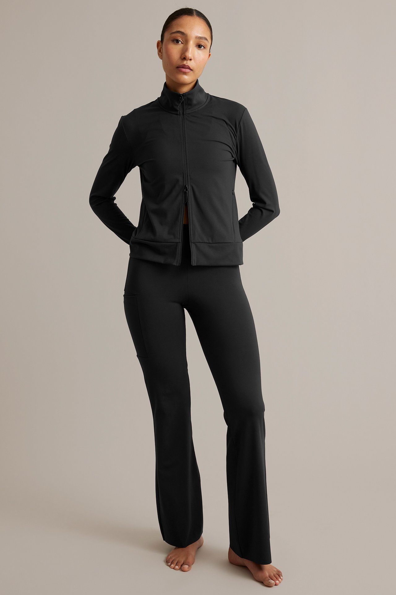 Edestä: nainen yllään musta treenitakki vetoketjulla ja mustat treenihousut.