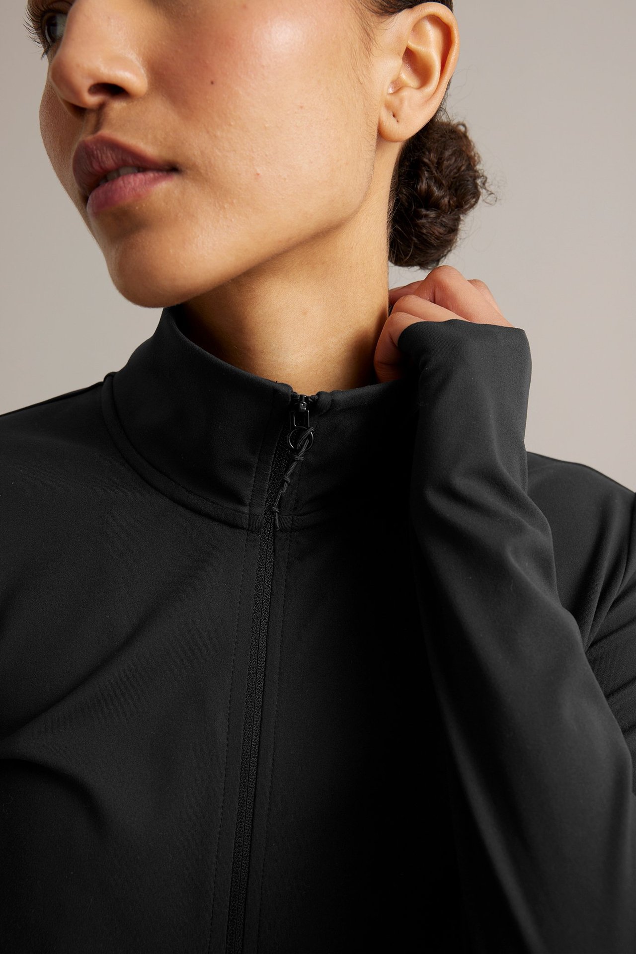 Närbild på en kvinna som bär en svart, högkragen träningsjacka med hel dragkedja och tumhål.