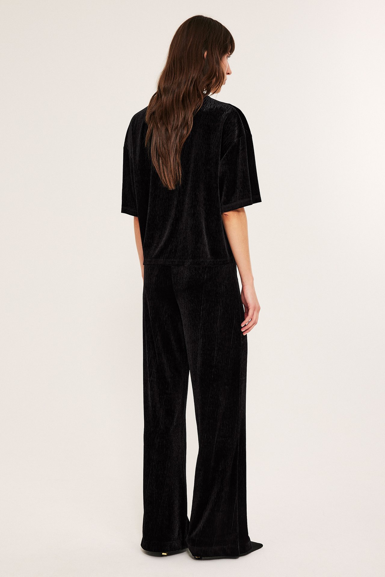 Kvinne i svarte veloursbukser med vide ben, sett bakfra.