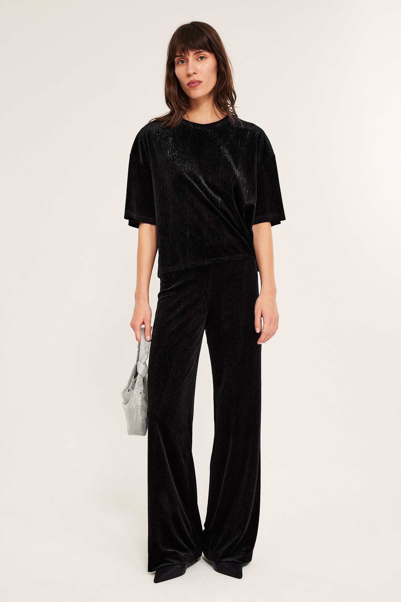 Kvinne i svarte fløyelsbukser med vide ben, frontvisning.