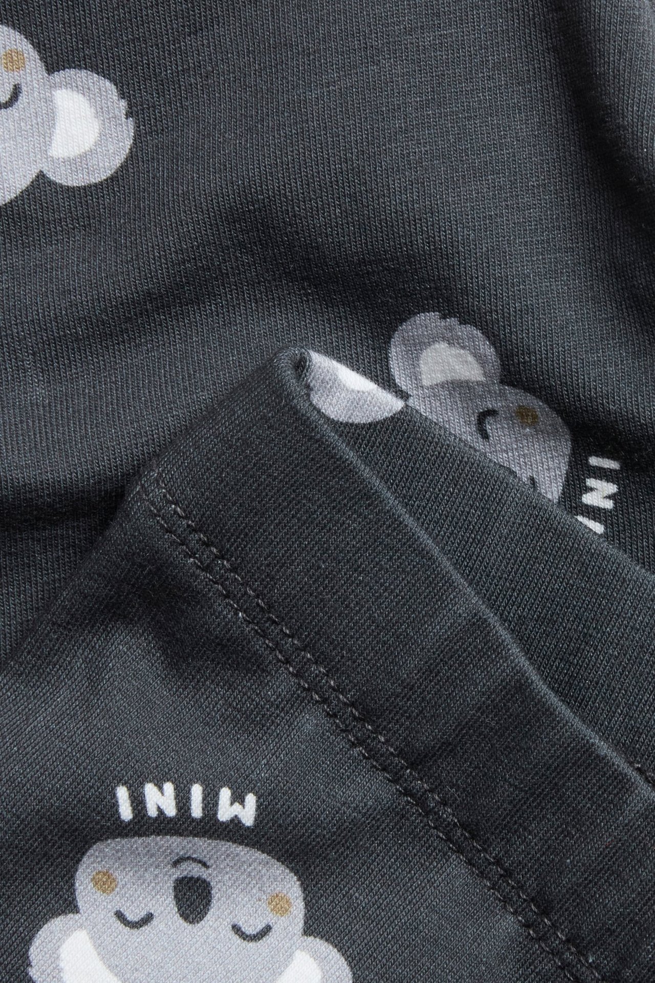 Zbliżenie na ciemnoszare legginsy z dżerseju z nadrukiem koali i widocznymi szwami na złożonym materiale.