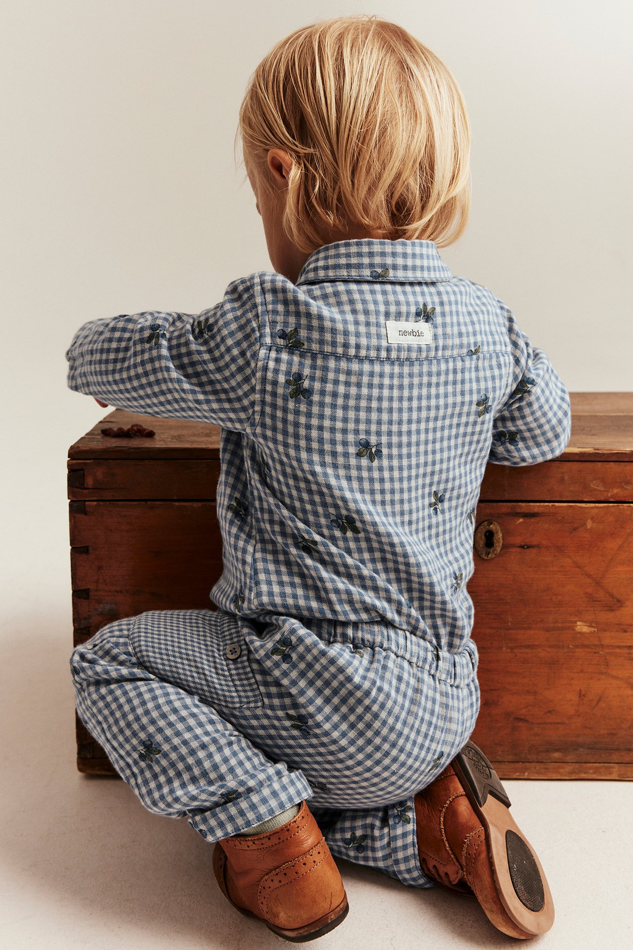 Bakfra: Barn i blårutete bomulls skjortebody med blåbærtrykk og brune sko.