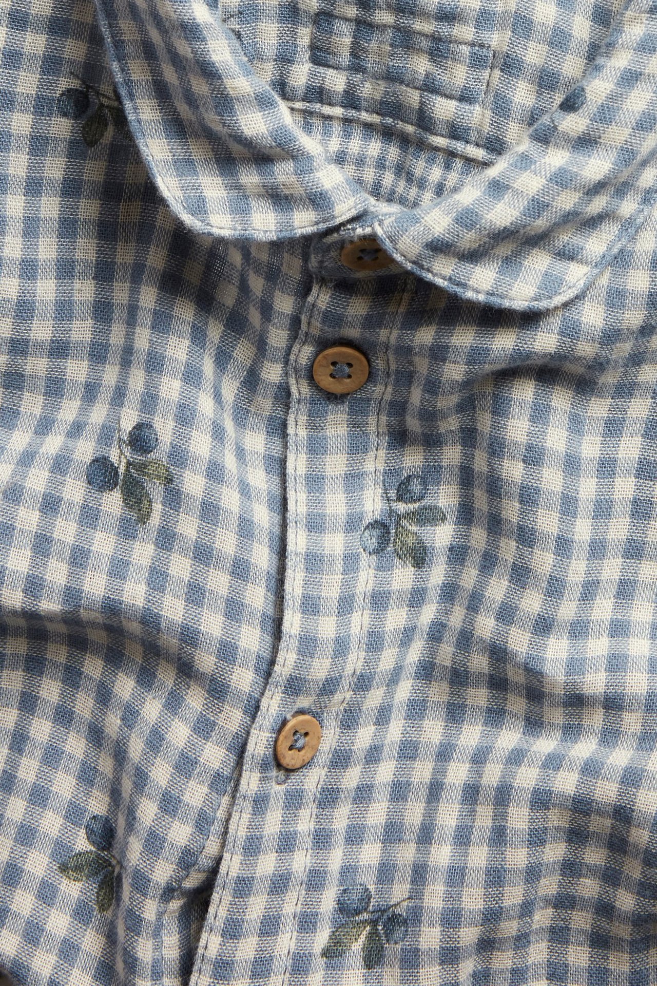 Zbliżenie na niebiesko-białe bawełniane body w kratkę z kołnierzykiem, drewnianymi guzikami i nadrukiem jagód.