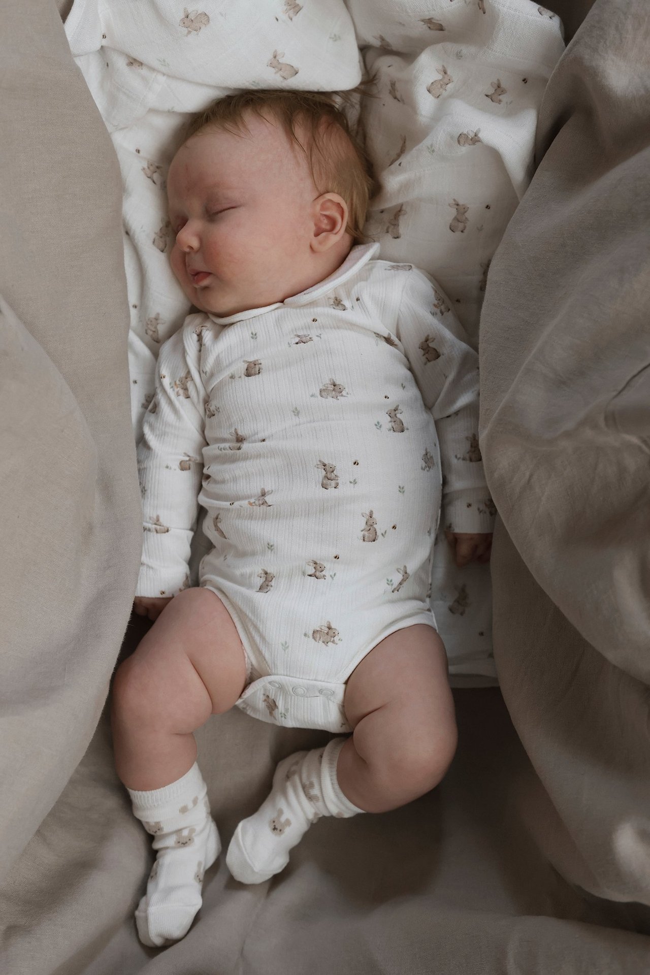 Ovenfra, sovende baby i en offwhite ribbet langermet body med kanintrykk og matchende sokker.