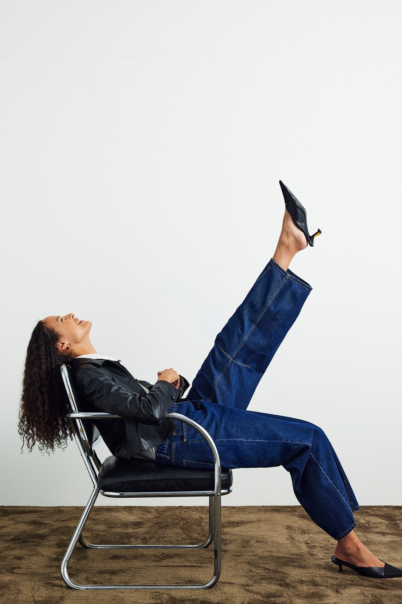 Sidebilde: kvinne i mørkeblå barrel-fit jeans, svart jakke, hvit skjorte og svarte mules.