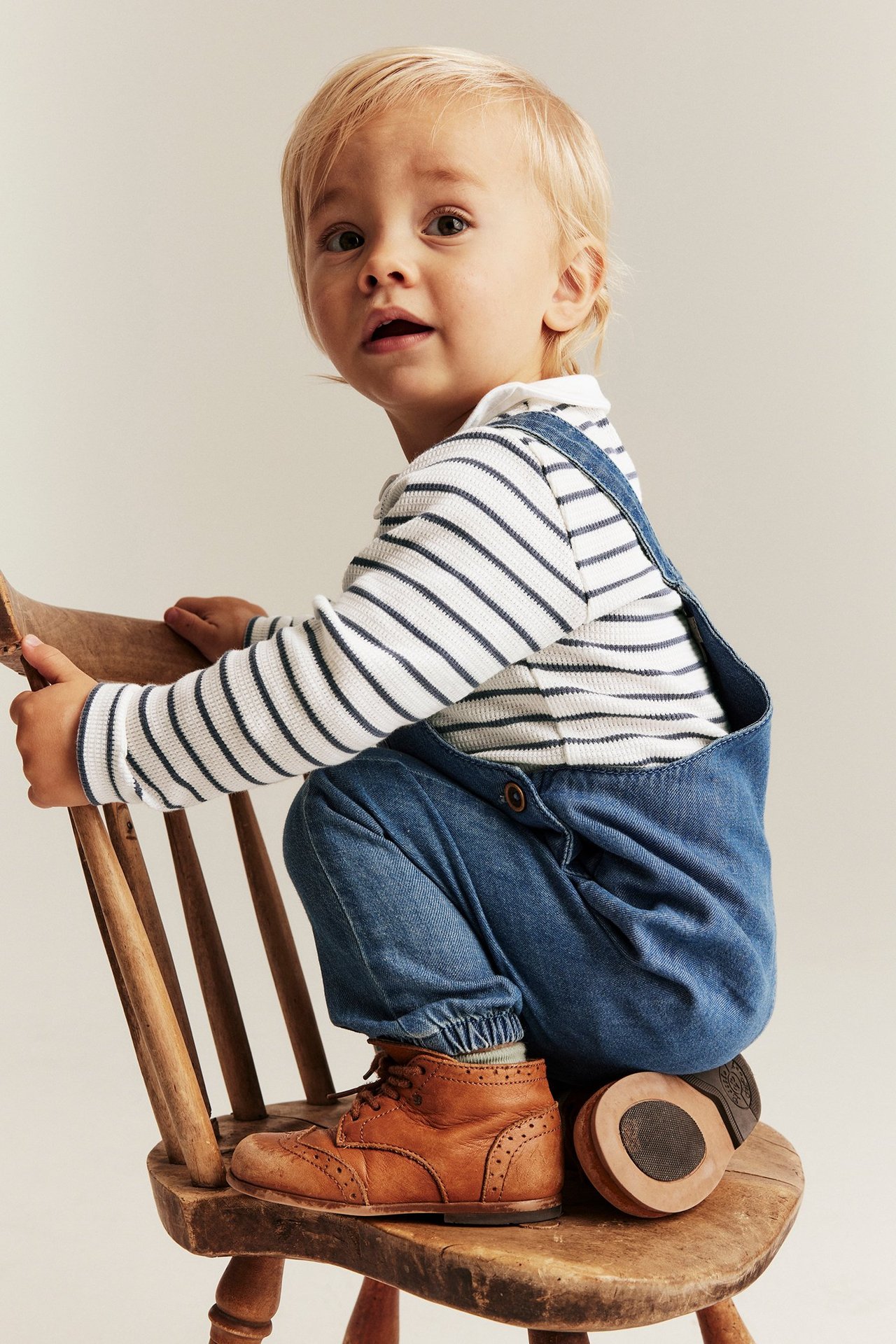 Vauva, sivukuva: luonnonvalkoinen raidallinen ribattu pitkähihainen kaulusbody, siniset denim-haalarihousut, ruskeat saappaat.