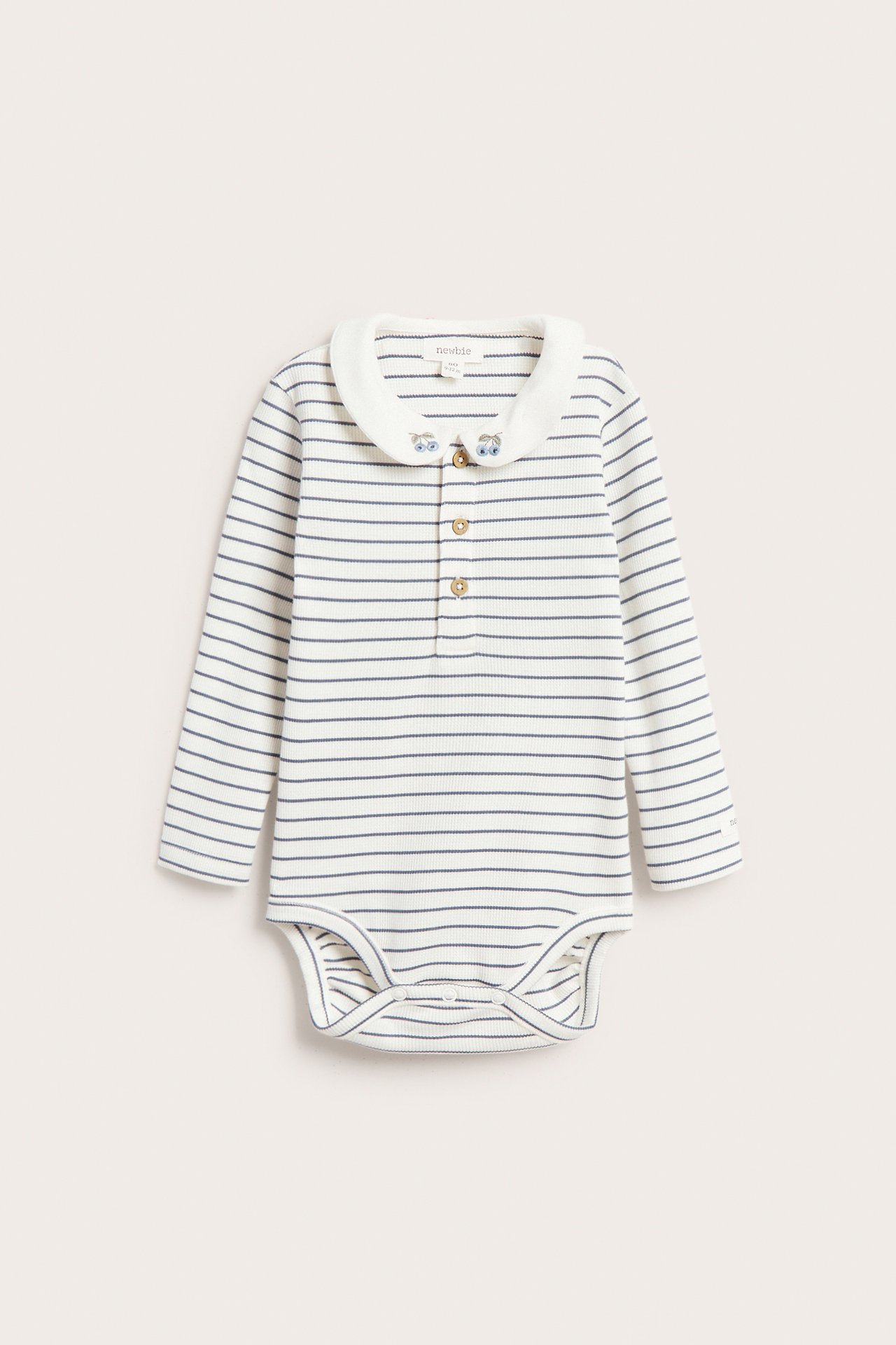 Edestä näkymä raidallisesta luonnonvalkoisesta ribbineulebodysta pitkillä hihoilla, brodeeratulla kauluksella ja nappikiinnityksellä.