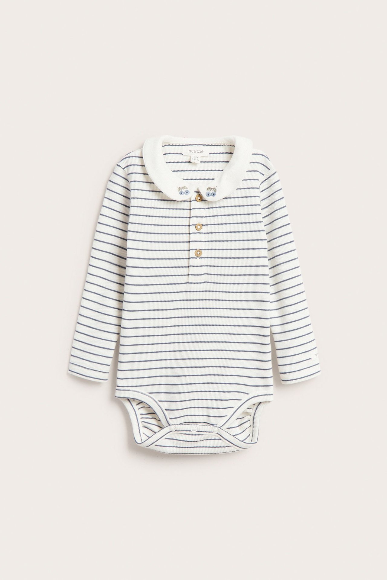 Edestä näkymä raidallisesta luonnonvalkoisesta ribbineulebodysta pitkillä hihoilla, brodeeratulla kauluksella ja nappikiinnityksellä.