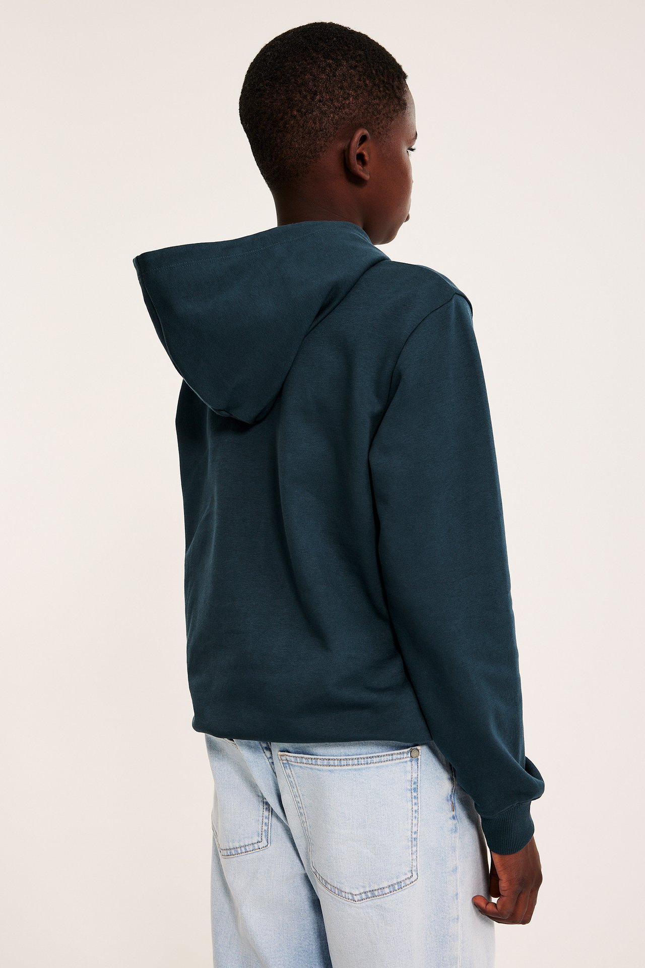 Widok z tyłu dziecka w ciemnoniebieskiej bluzie z kapturem i jasnoniebieskich jeansach.