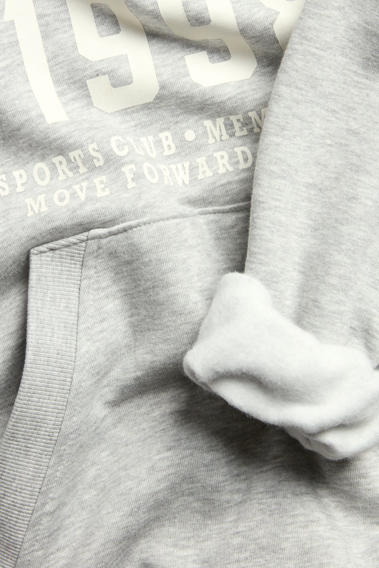 Zbliżenie szarej melanżowej bluzy z kapturem: biały nadruk, kieszeń kangurka i miękkie, szczotkowane wnętrze.