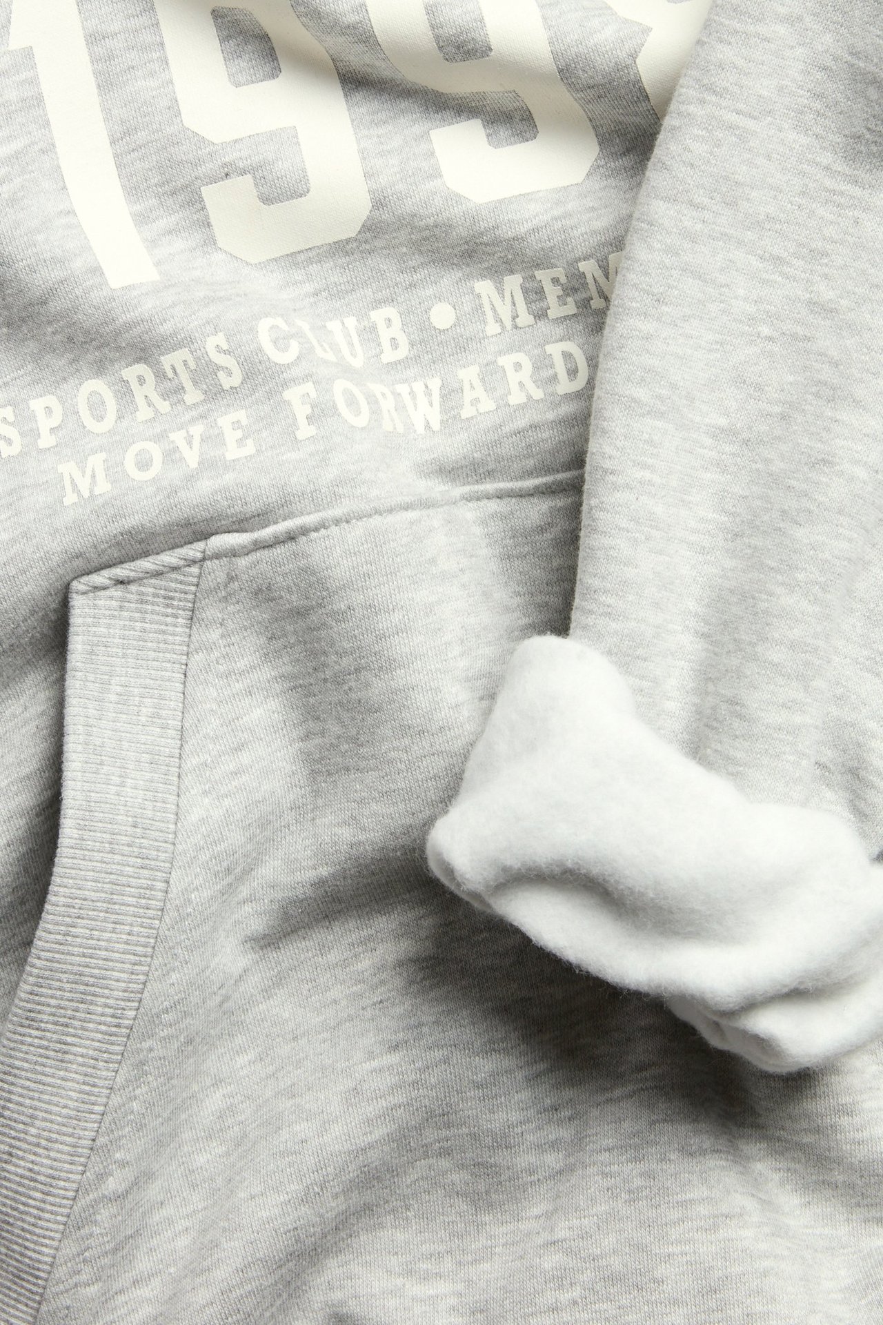 Zbliżenie szarej melanżowej bluzy z kapturem: biały nadruk, kieszeń kangurka i miękkie, szczotkowane wnętrze.