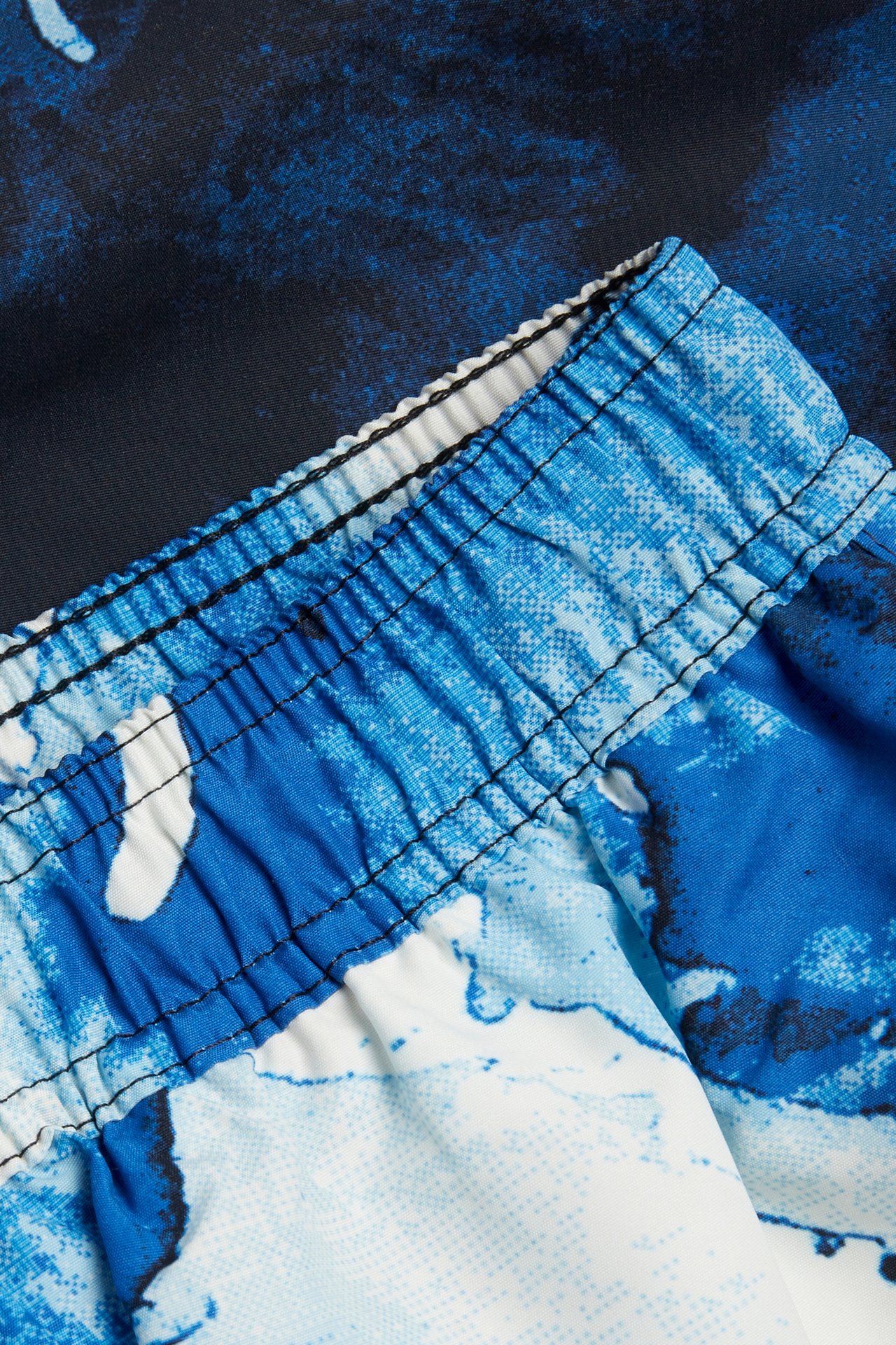 Närbild av badshorts med resårlinning och ett abstrakt mönster i blått och offwhite.