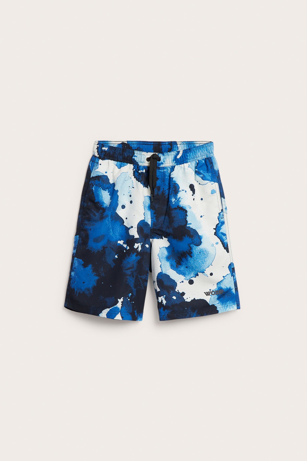 Framifrån: barnens offwhite badshorts med abstrakt blått stänkmönster, fickor och svart dragsko i midjan.