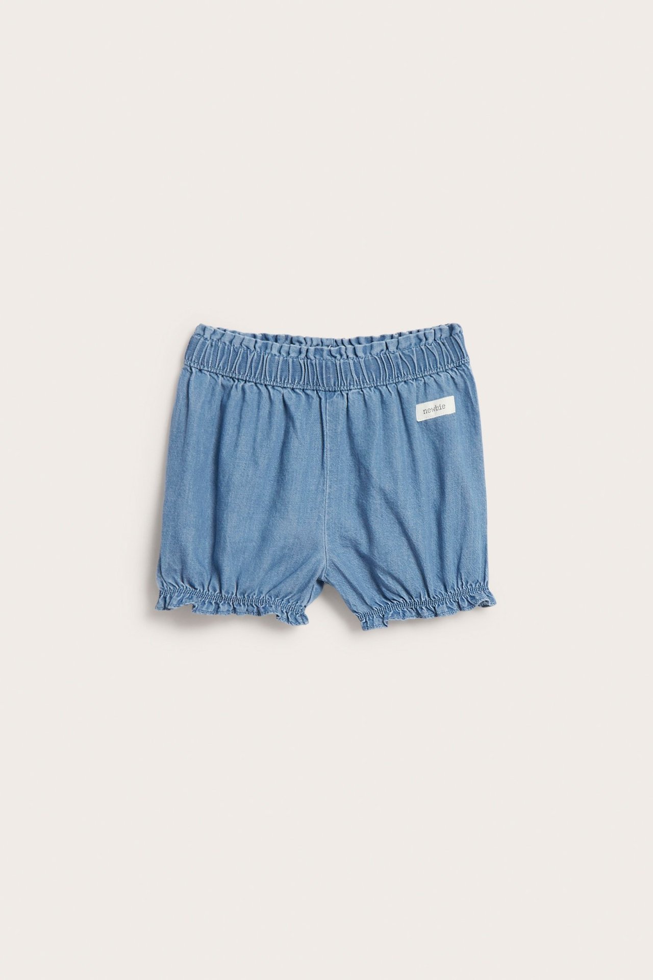 Frontbilde av lyse denimshorts for baby med elastisk midje og rynker i benåpningene.