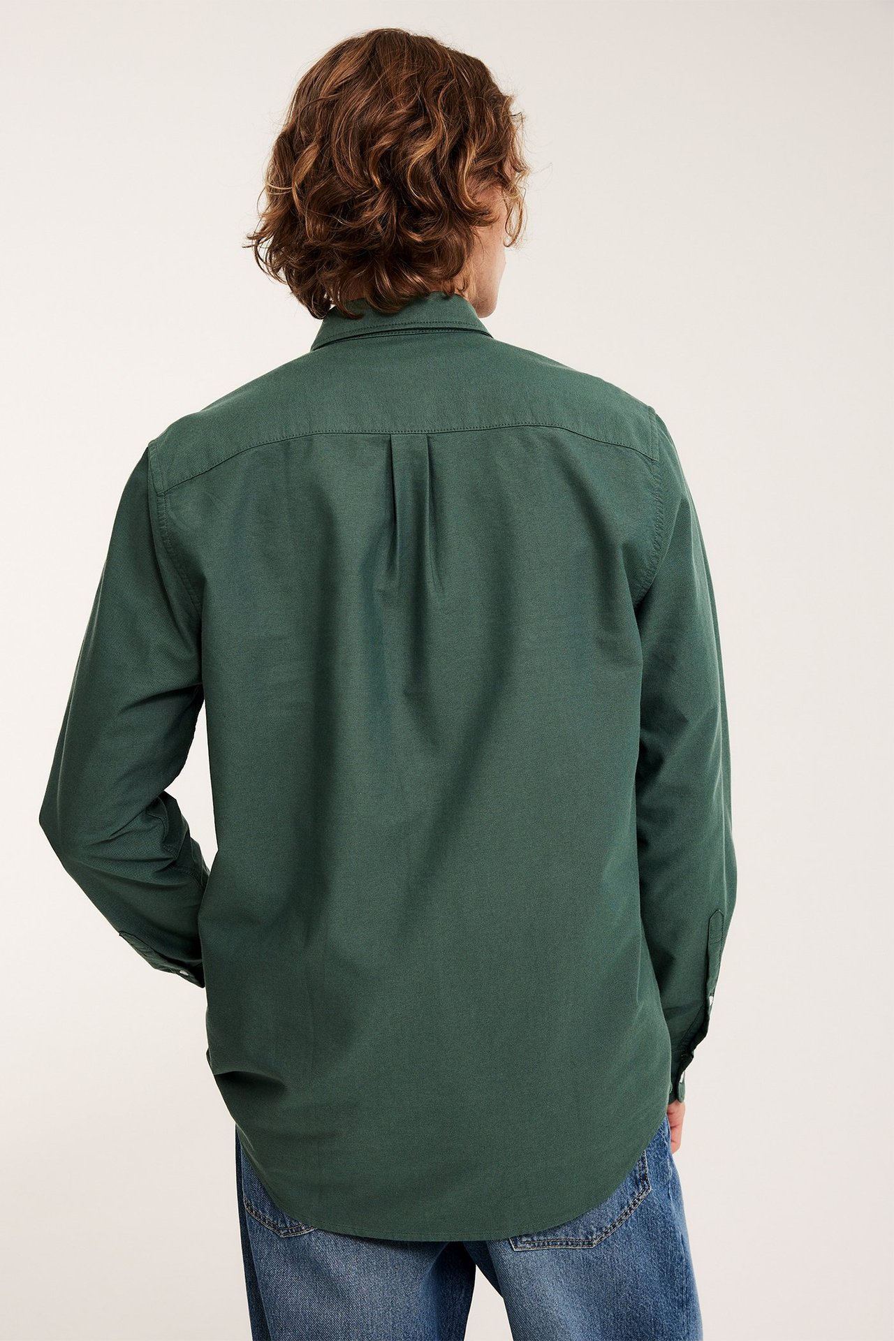 Bakifrån på en man i en grönmelerad regular fit oxfordskjorta i bomull och blå jeans.