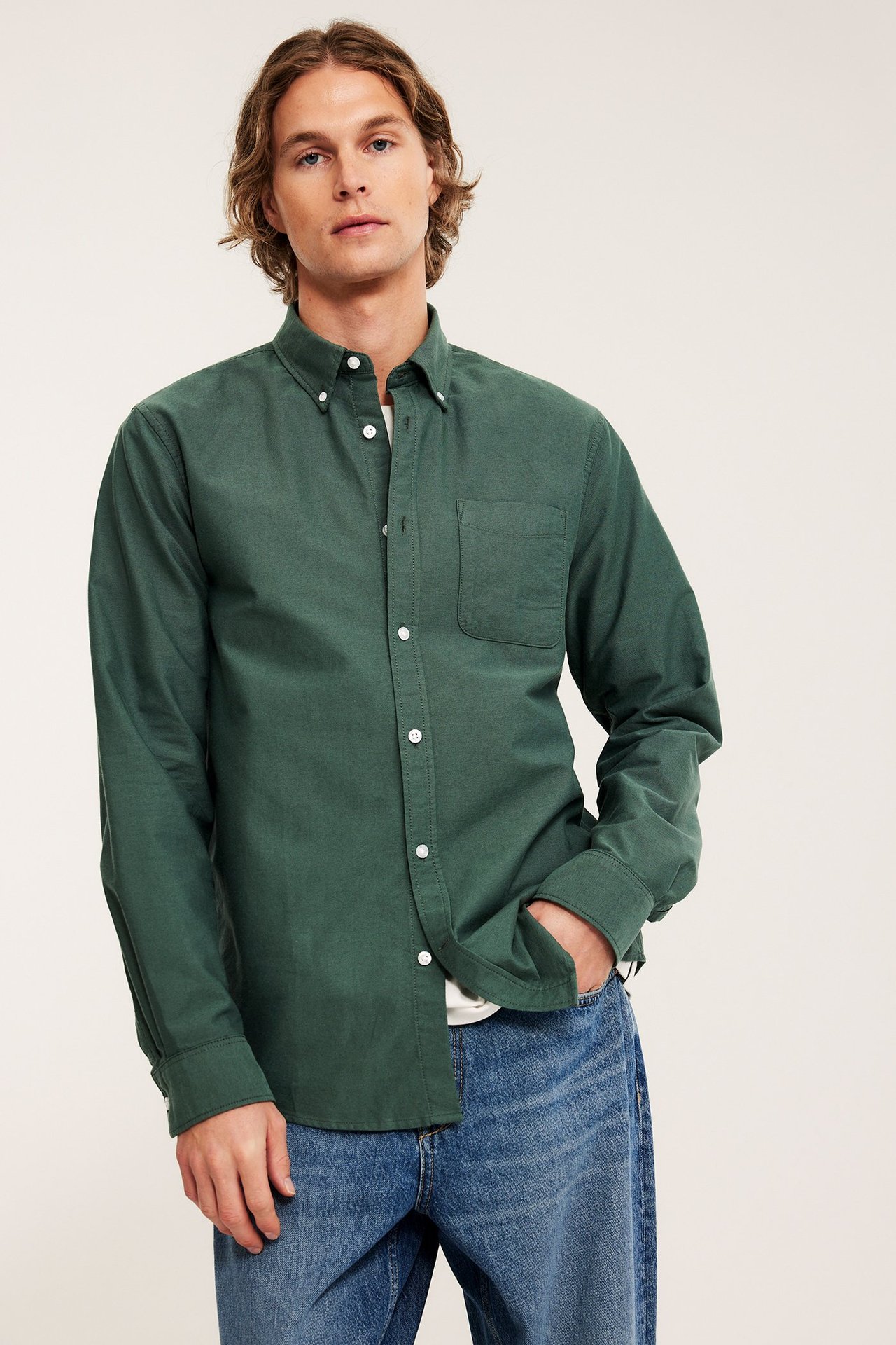 Framifrån man i grön melerad regular fit oxfordskjorta i bomull över vit t-shirt och blå jeans.
