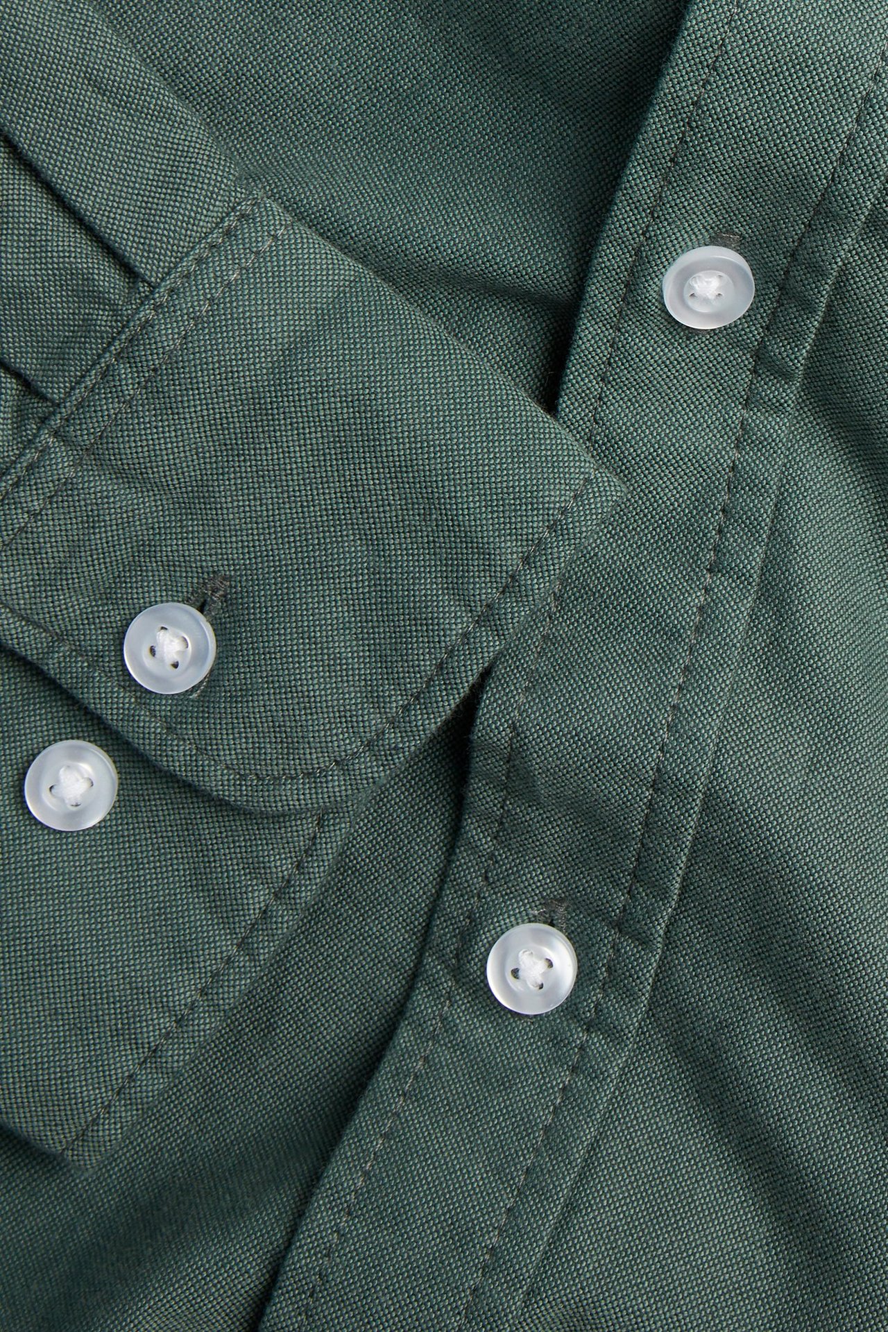 Lähikuva vihreästä meleeratusta Oxford-miestenpaidasta valkoisilla napeilla kauluksessa ja napituslistassa.