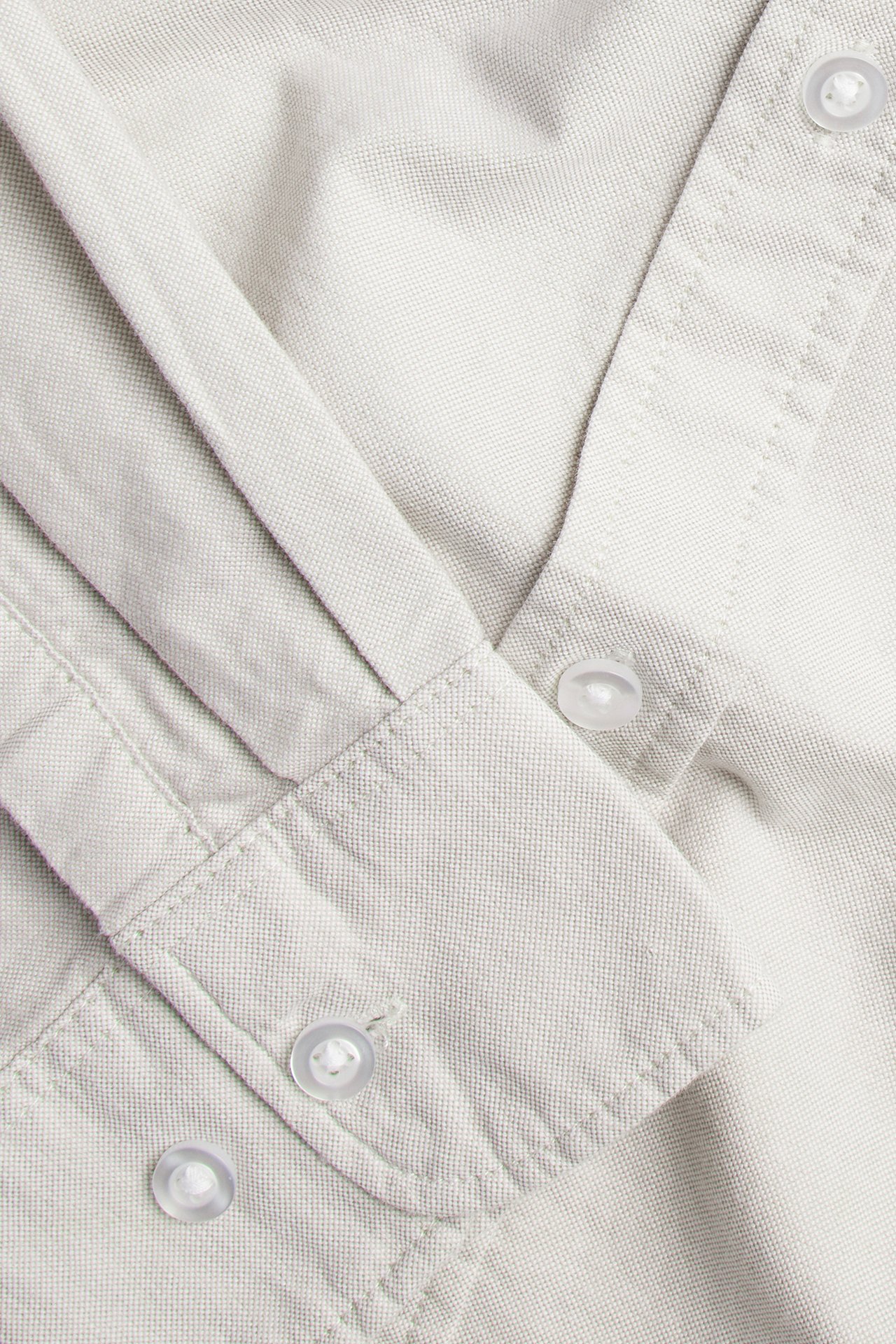 Lähikuva vaaleanbeigestä meleeratusta puuvillaisesta Oxford-paidasta, jossa on nappikaulus ja kaksinnappinen ranneke.