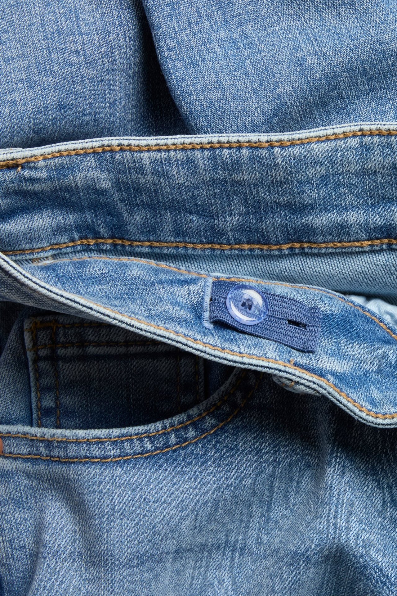 Zbliżenie na niebieskie jeansy bootcut z niskim stanem, z regulowaną gumką i przezroczystym guzikiem.