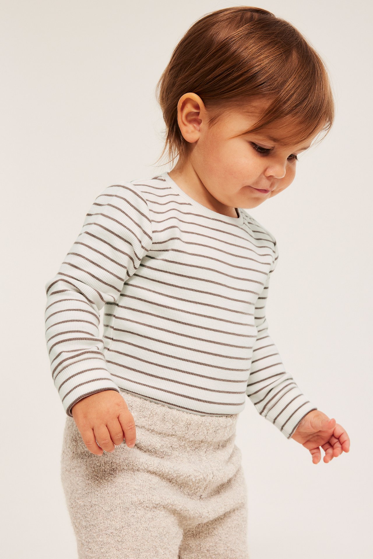 Edestäpäin: Vauva luonnonvalkoisessa ribbihaalareissa ja beigeissä neulotuissa housuissa.