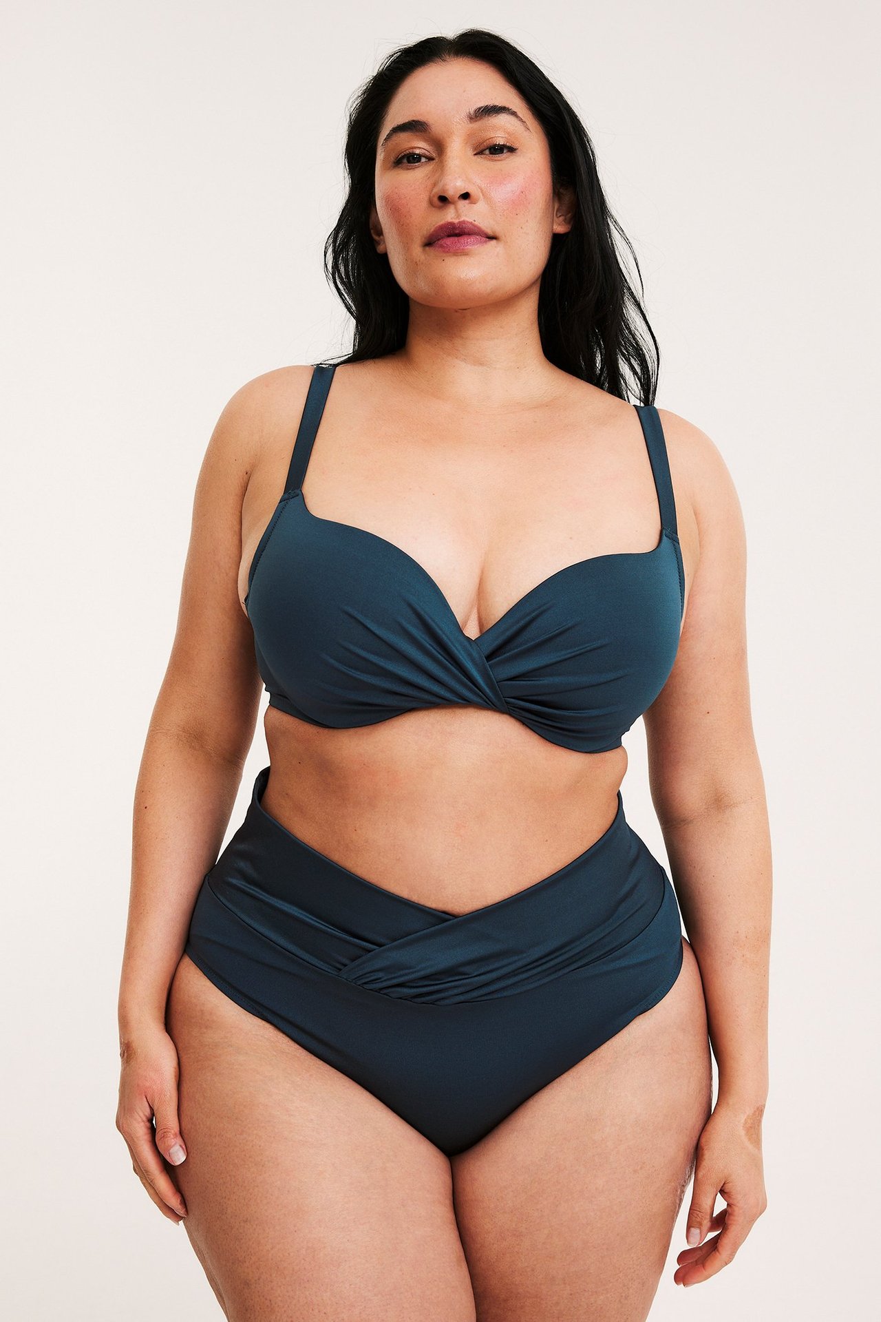 Edestä kuvattuna nainen yllään tummansininen bikinin yläosa kierretyllä etuosalla ja yhteensopivat korkeavyötäröiset alaosat.