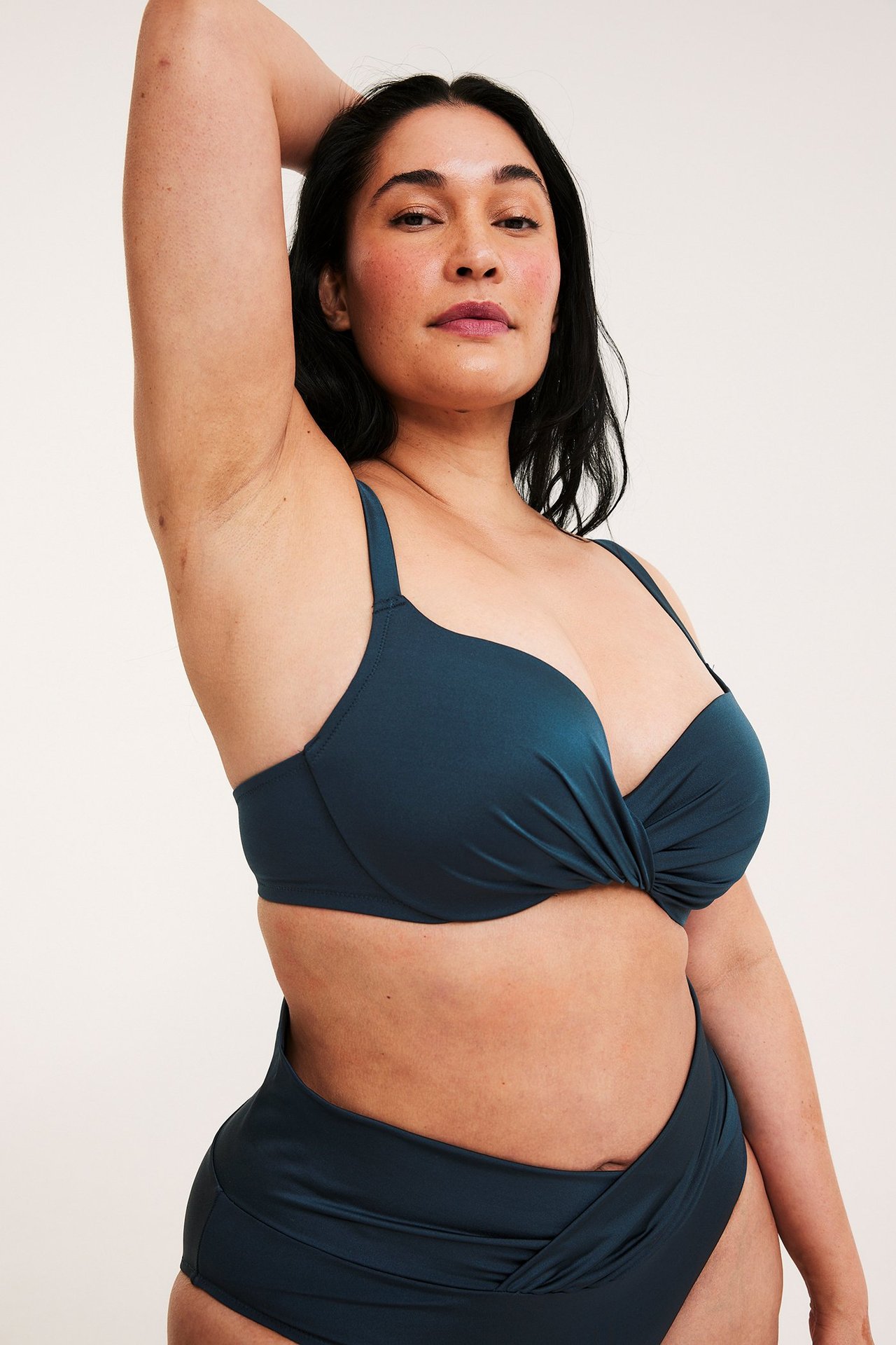 Lähikuva naisesta tummansinisessä bikiniliivissä kierretyllä etuosalla ja yhteensopivilla korkeilla alaosilla.