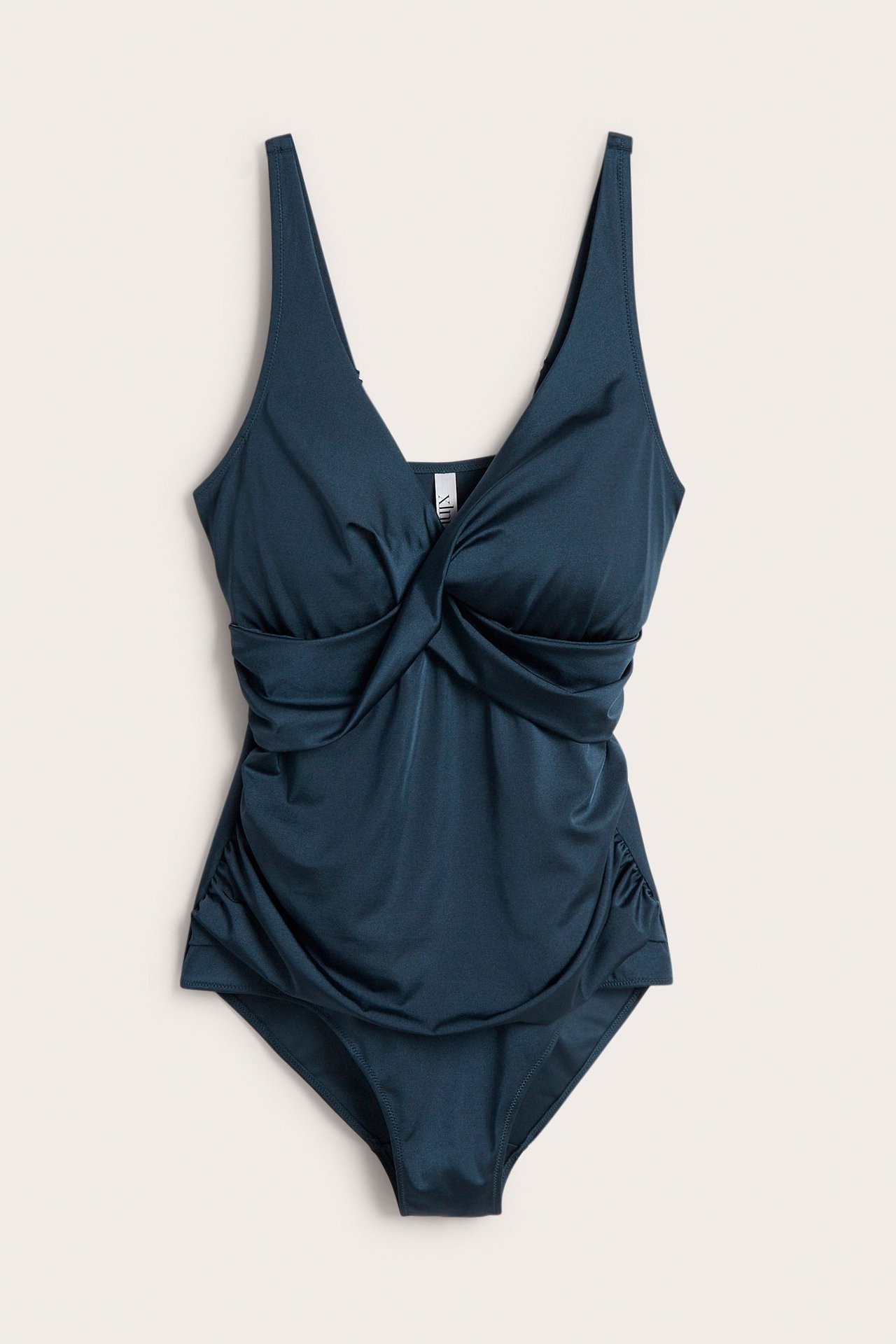 Forfra mørkeblå, ensfarget badedrakt med drapert omslagssnitt og justerbare skulderstropper.