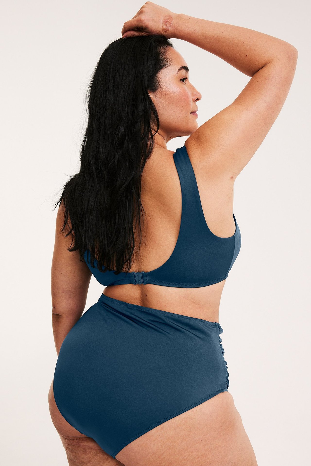 Sivukuva naisesta tummansinisissä korkeavyötäröisissä bikinialaosissa sivurypytyksin ja yhteensopivassa yläosassa.