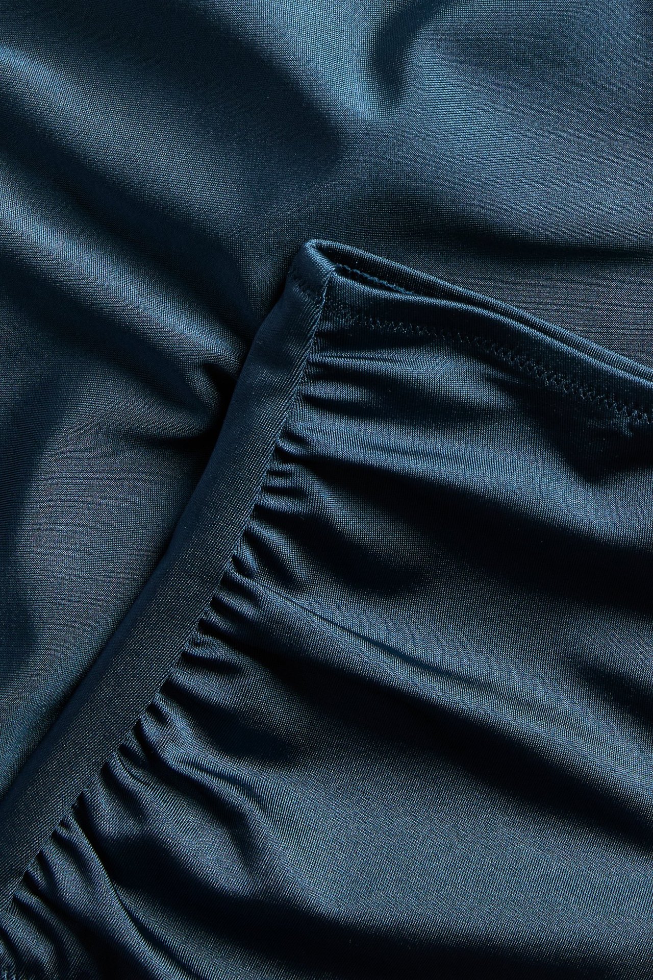 Zbliżenie na granatowe, jednolite majtki kąpielowe z wysokim stanem, marszczeniem po bokach i lekkim modelowaniem.