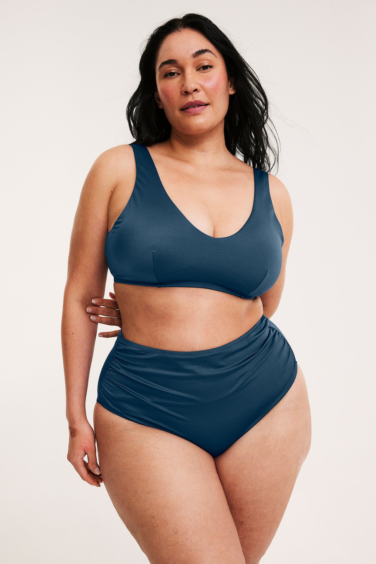 Etunäkymä: Nainen tummansinisissä korkeavyötäröisissä bikinihousuissa sivurypytyksillä ja yhteensopivalla yläosalla.