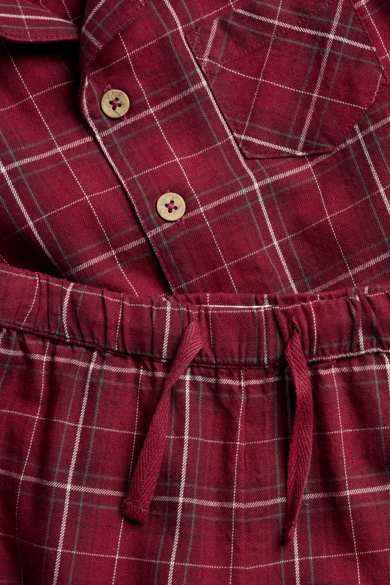 Närbild av en röd rutig flanellpyjamas med träknappar på skjortan och dragsko i byxorna.