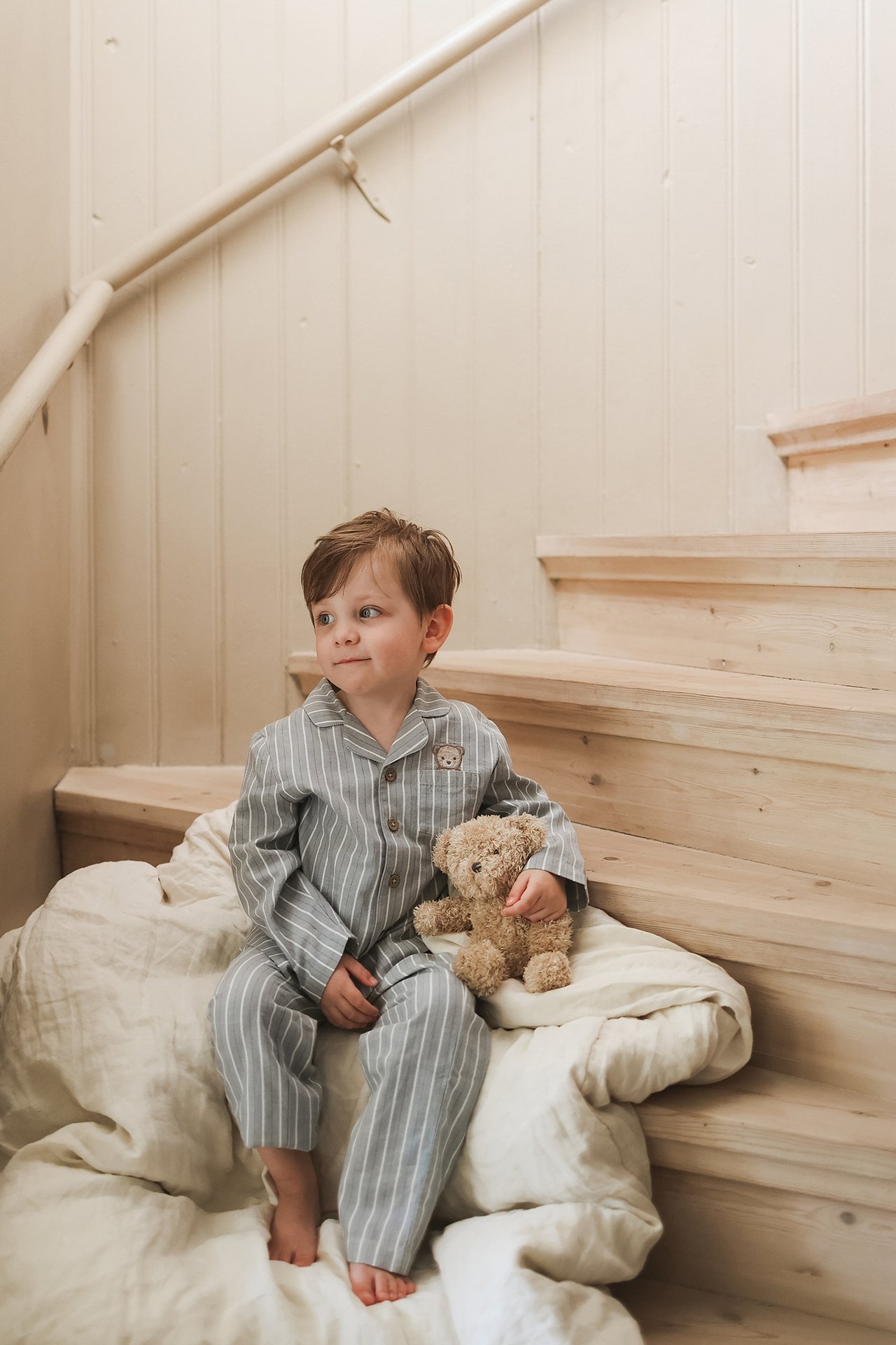 Widok z boku dziecka w jasnoniebieskiej piżamie bawełnianej w paski, trzyma brązowego misia.