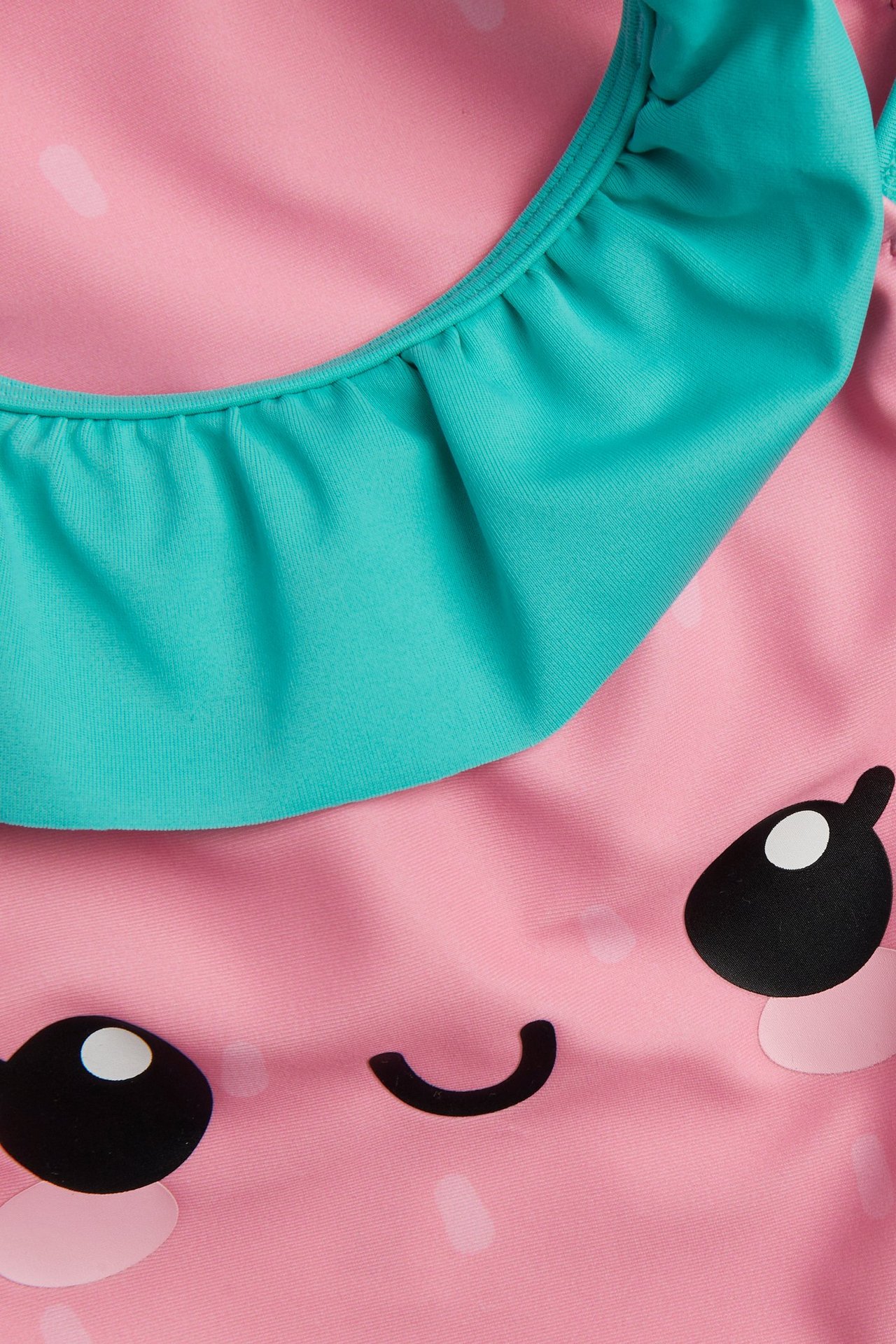 Lähikuva edestä: lasten pinkki mansikkakuvioinen uimapuku vihreällä röyhelöpääntöllä.