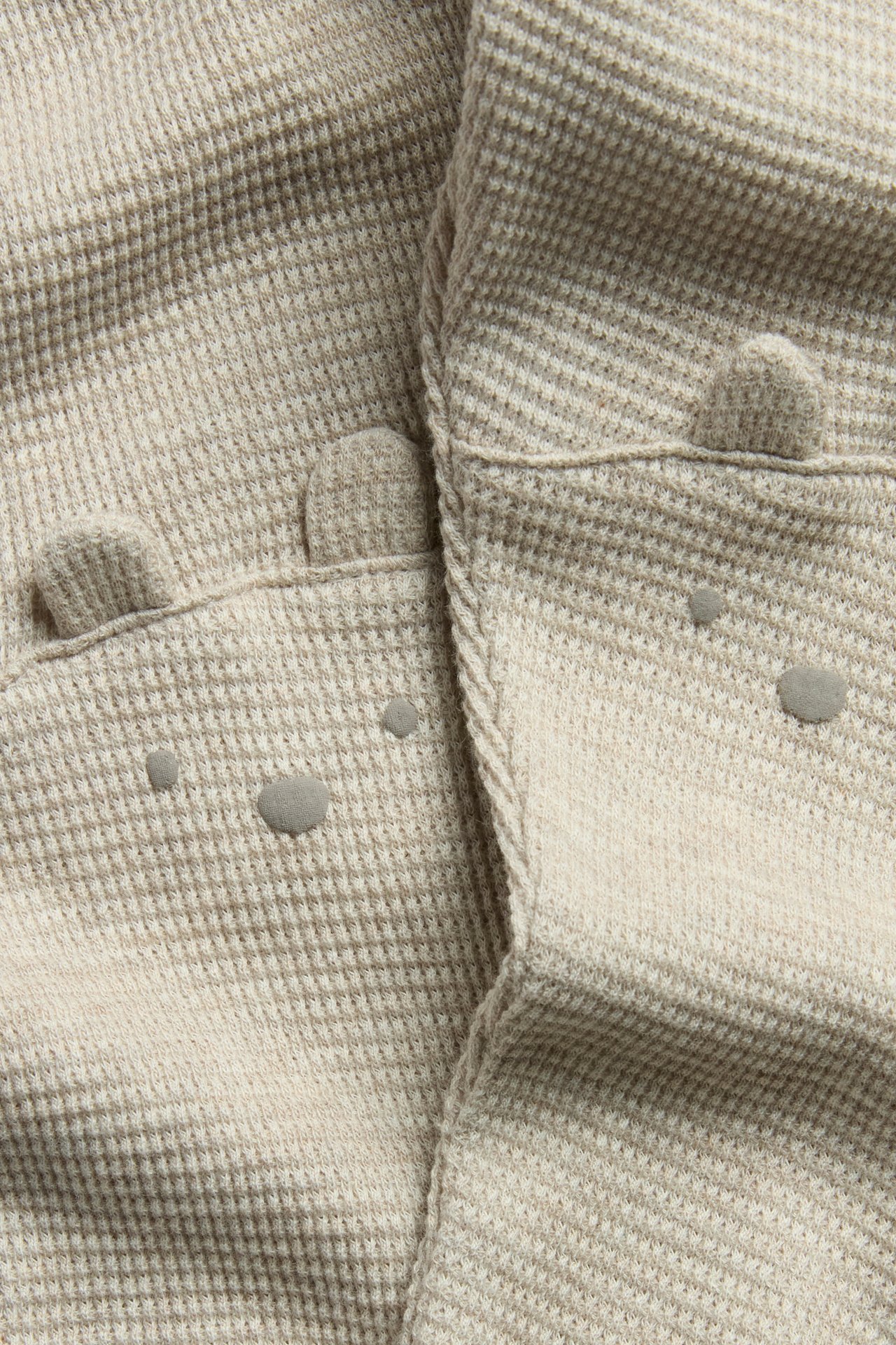 Nærbilde, forfra, av beigemelerte vaffelstrikkede leggings med bjørneansikter og fastsydde ører på knærne.