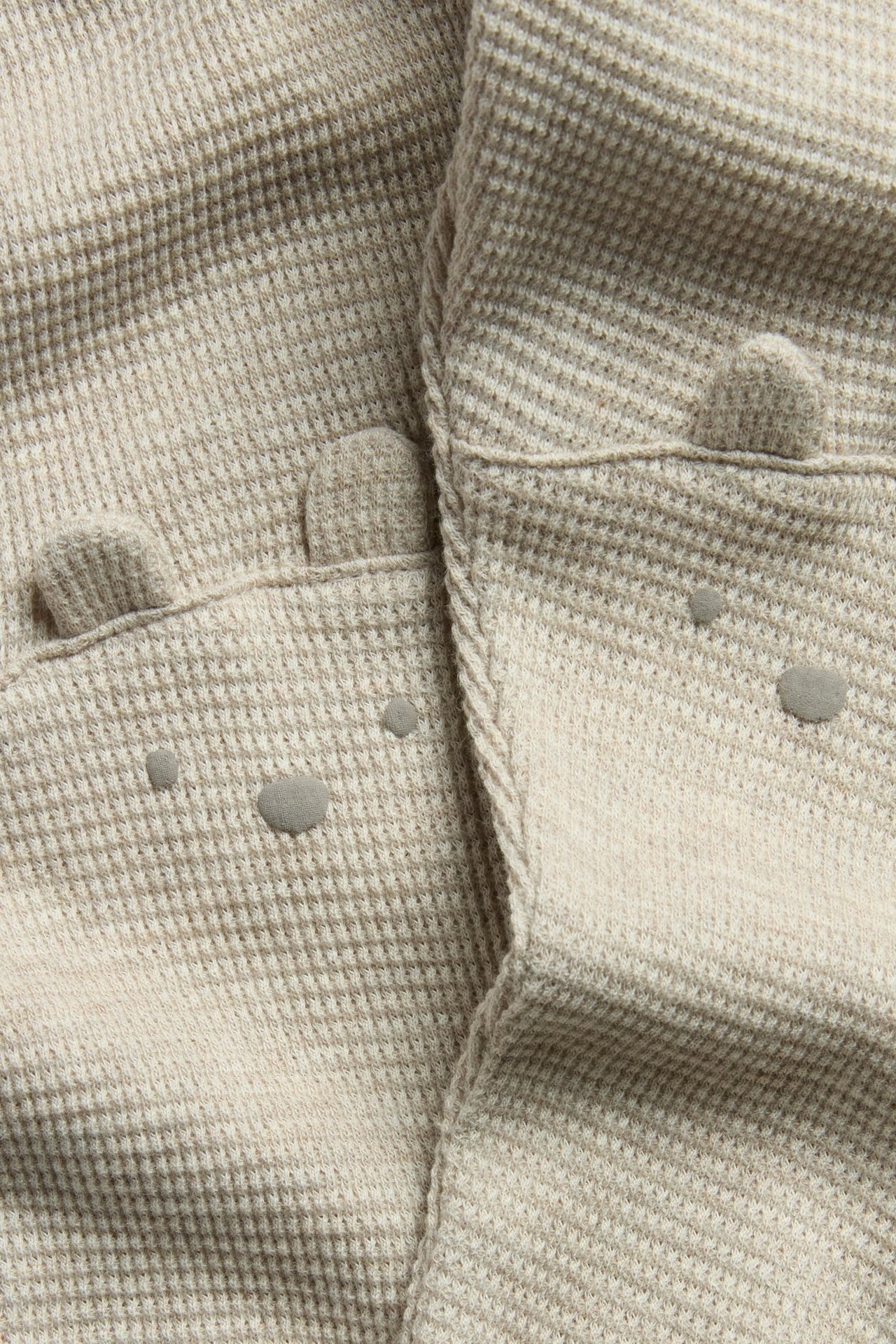 Zbliżenie: beżowe melanżowe legginsy waflowe z uszami i pyskami niedźwiedzia na kolanach.