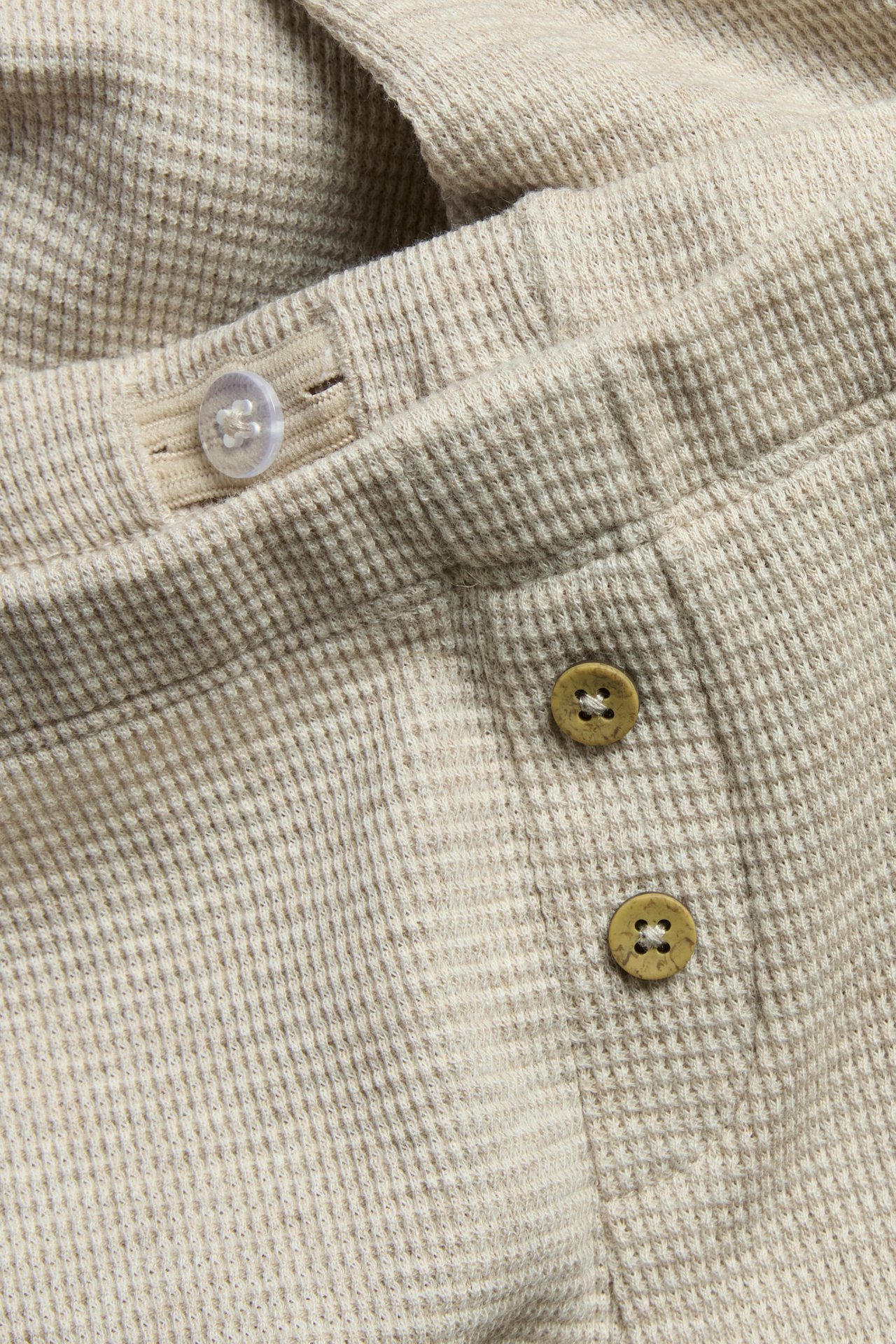 Zbliżenie beżowych legginsów o waflowej strukturze z ozdobnymi brązowymi i przezroczystymi guzikami.