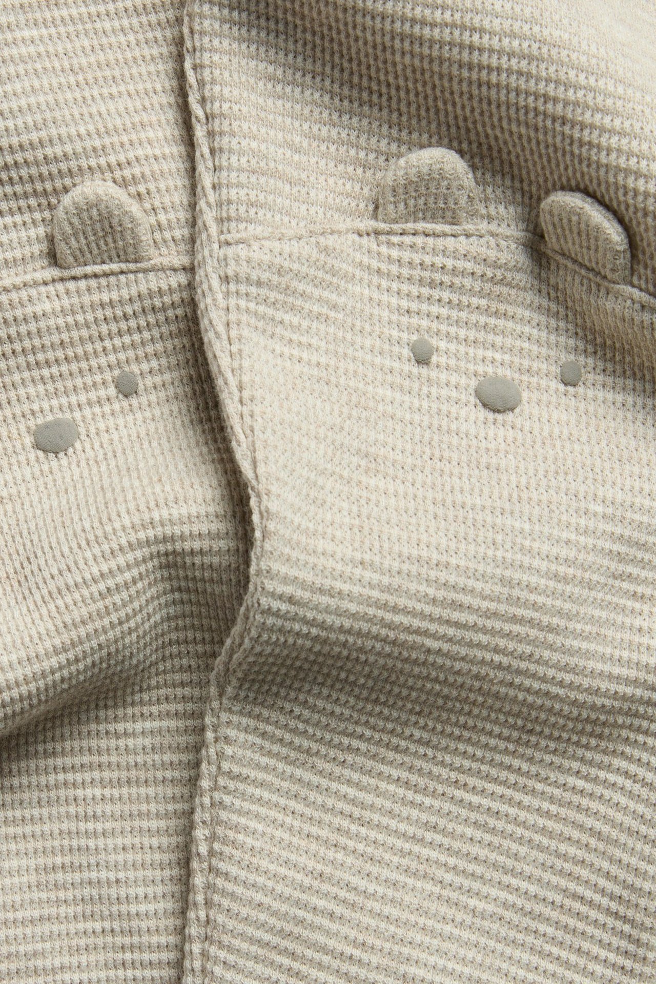 Zbliżenie beżowych melanżowych legginsów z dzianiny waflowej, ozdobnymi guzikami z przodu i małymi aplikacjami uszu.
