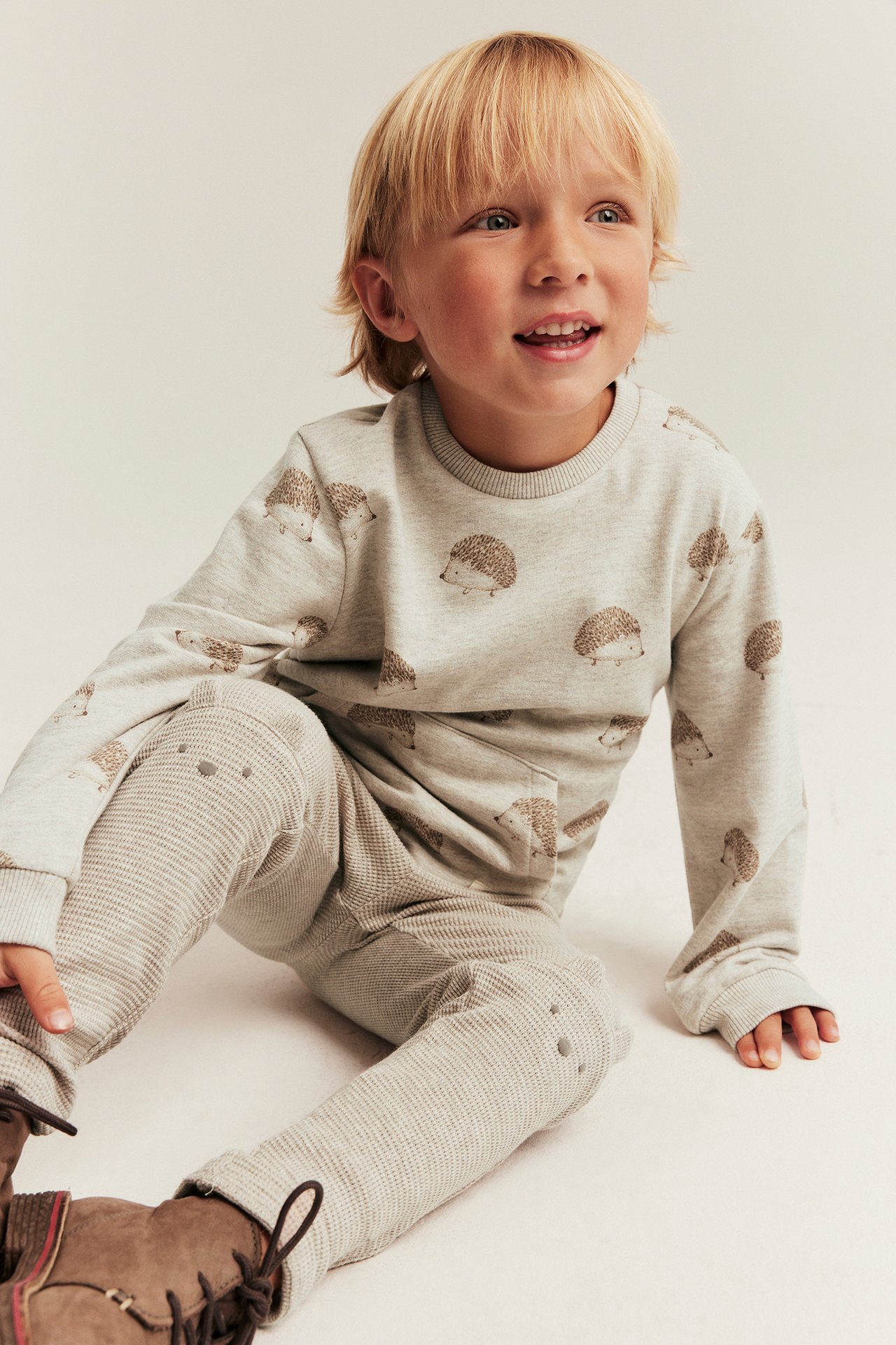 Frontvy: Kid bär beiga våffelstickade leggings med knäöron, prickmönster och en grå tröja med igelkottsmönster.