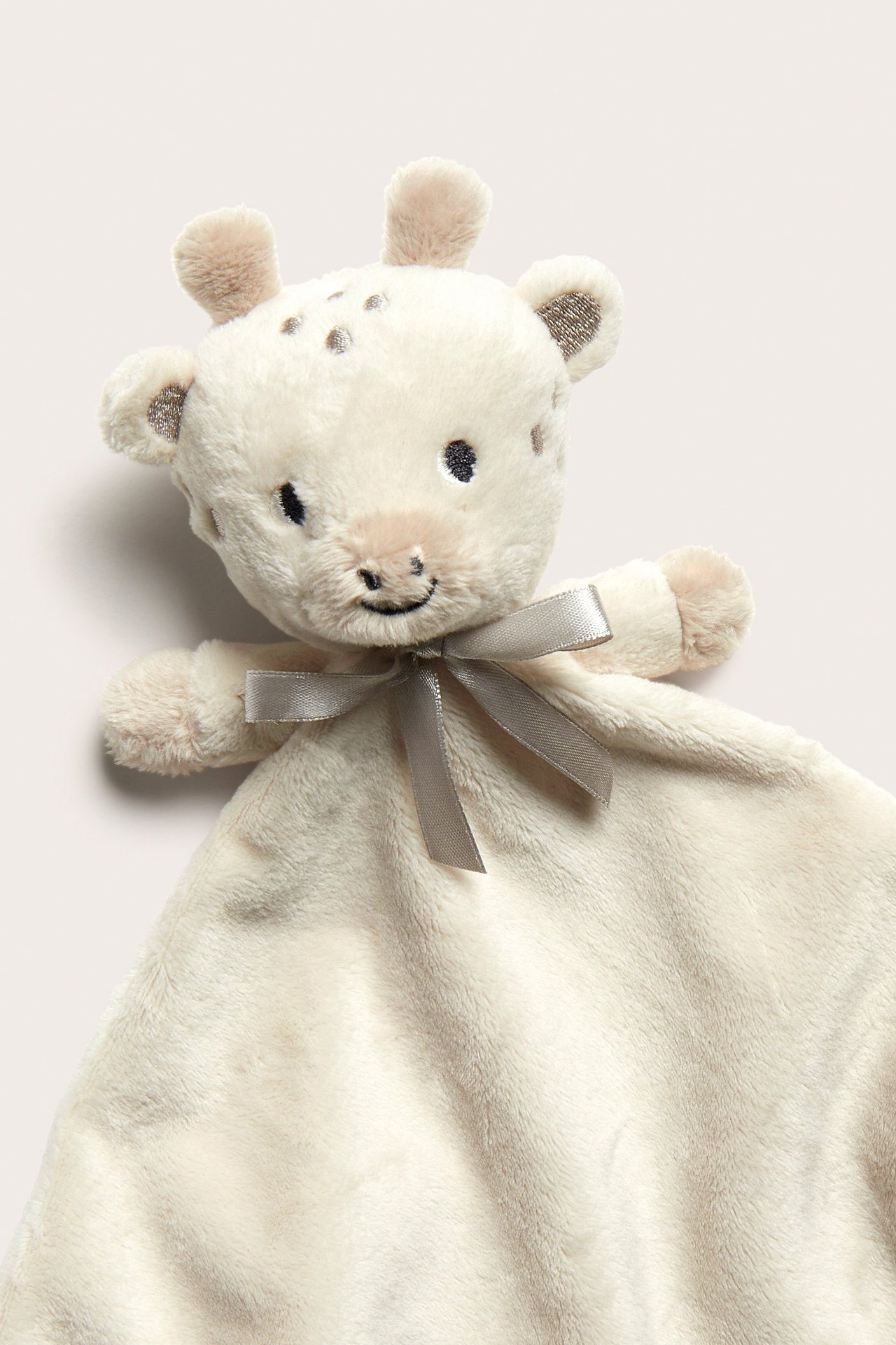 Nærbilde forfra: Lys beige, myk polyester giraff-koseteppe med en grå sløyfe.